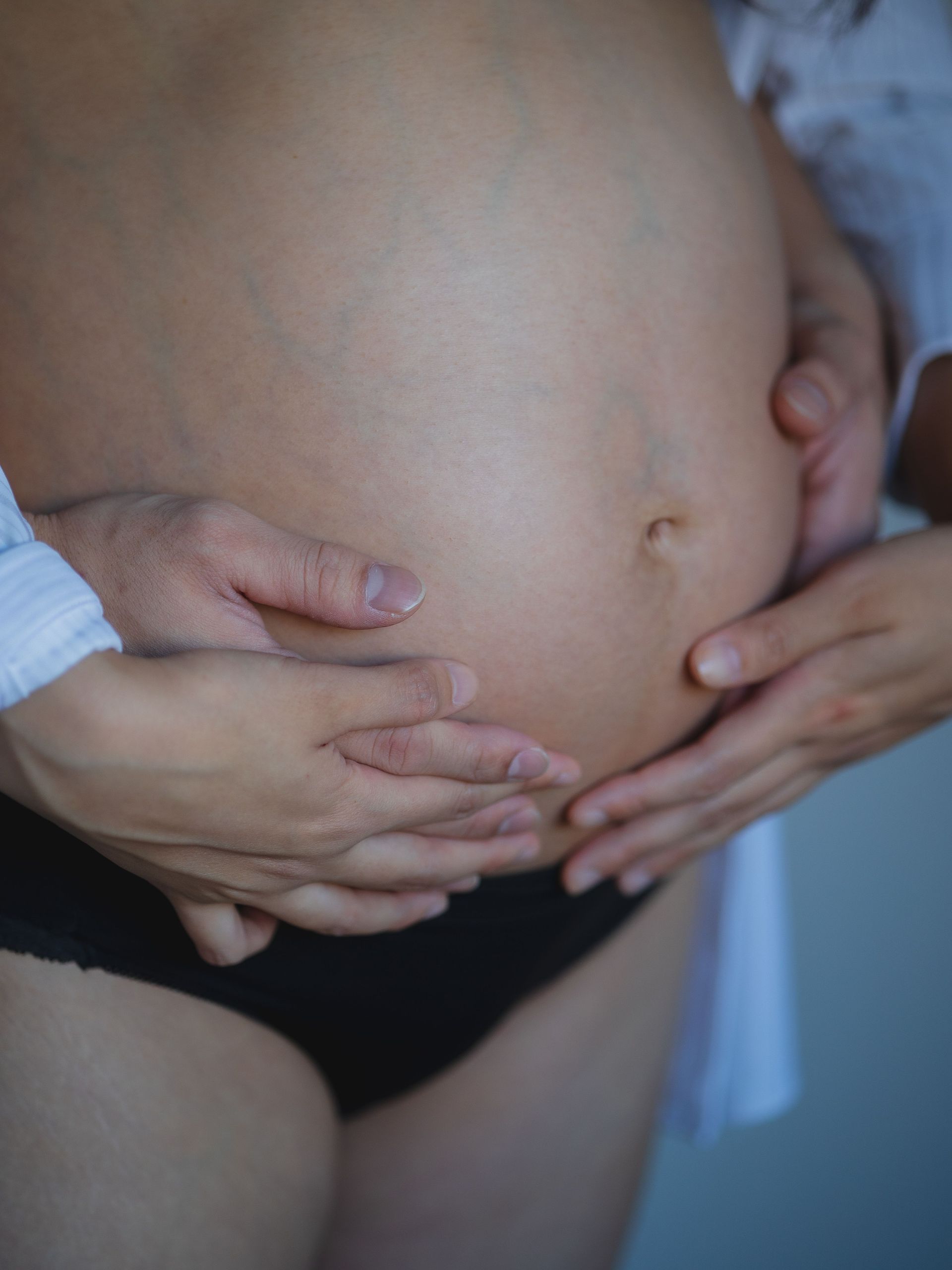 Close-up of a pregnant belly being gently held by two hands, with a black waistband visible.