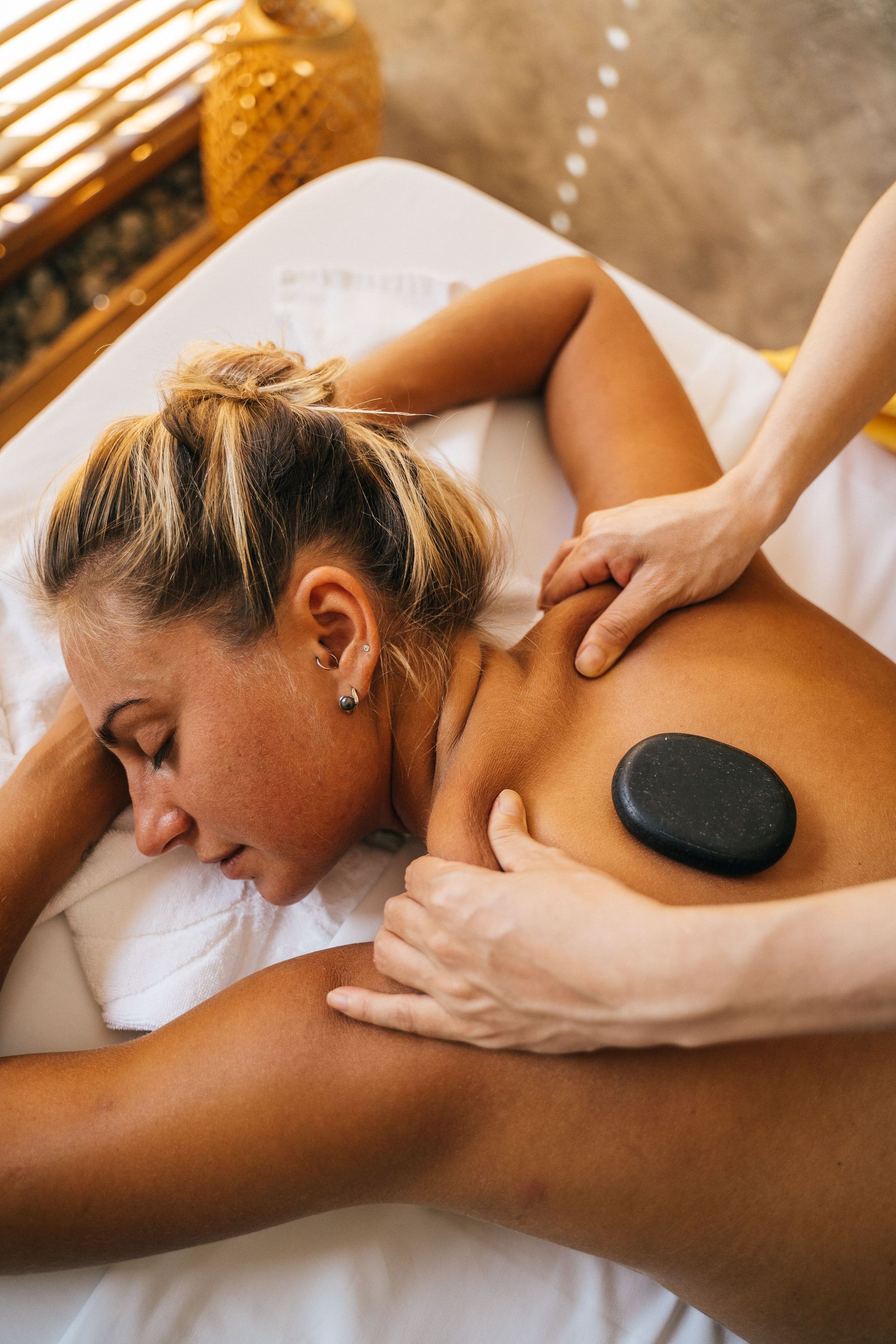Hot stone massage on a person’s back with white flowers nearby