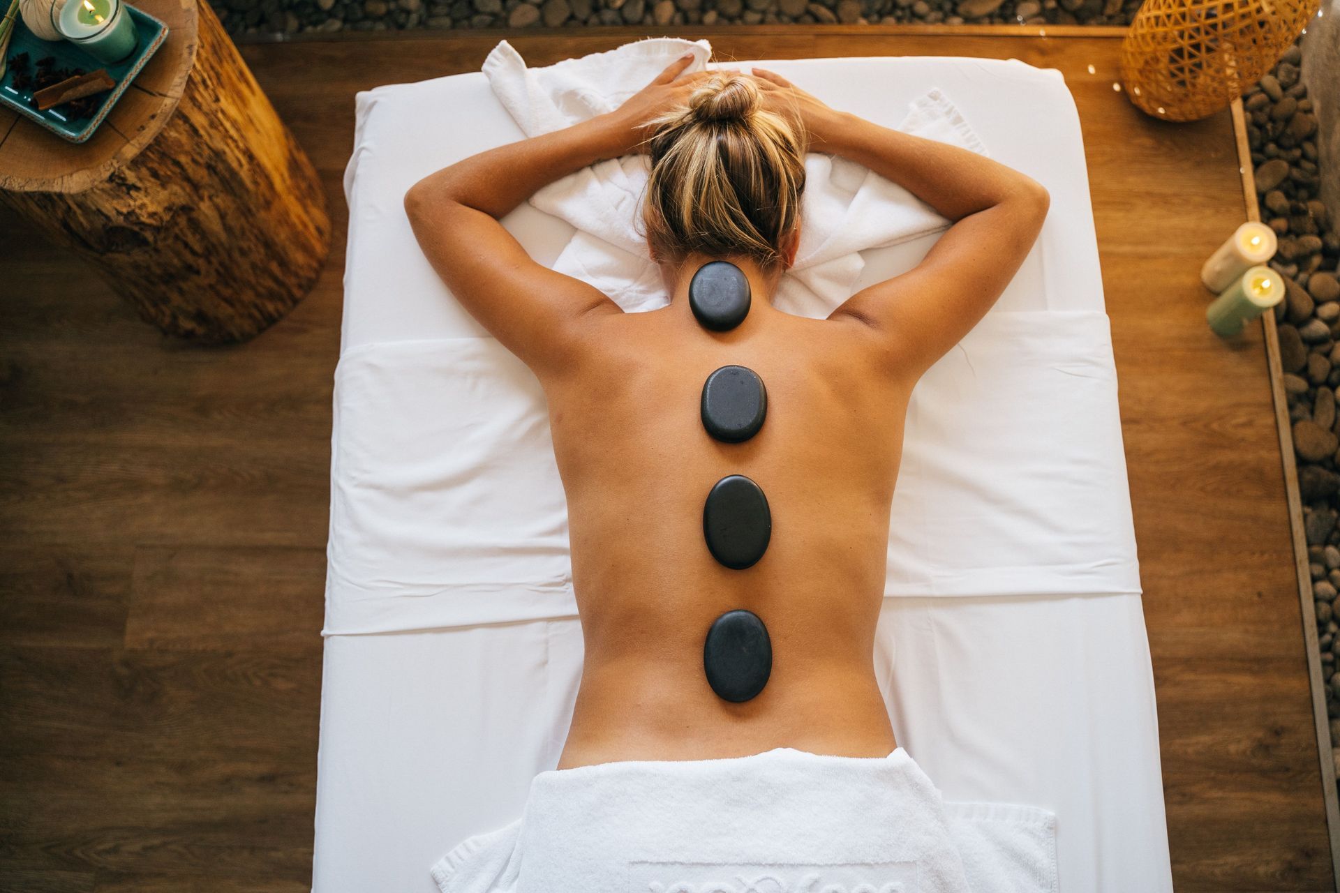 Person lying face down on a massage table with hot stones placed along the back