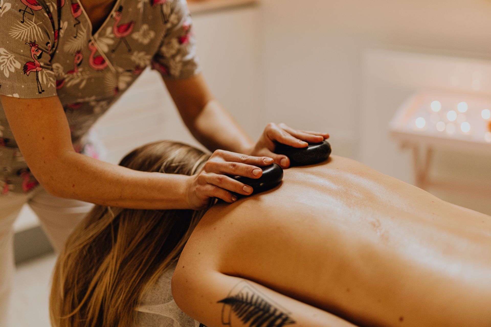 Massage therapist using hot stones on a client's bare back in a spa setting