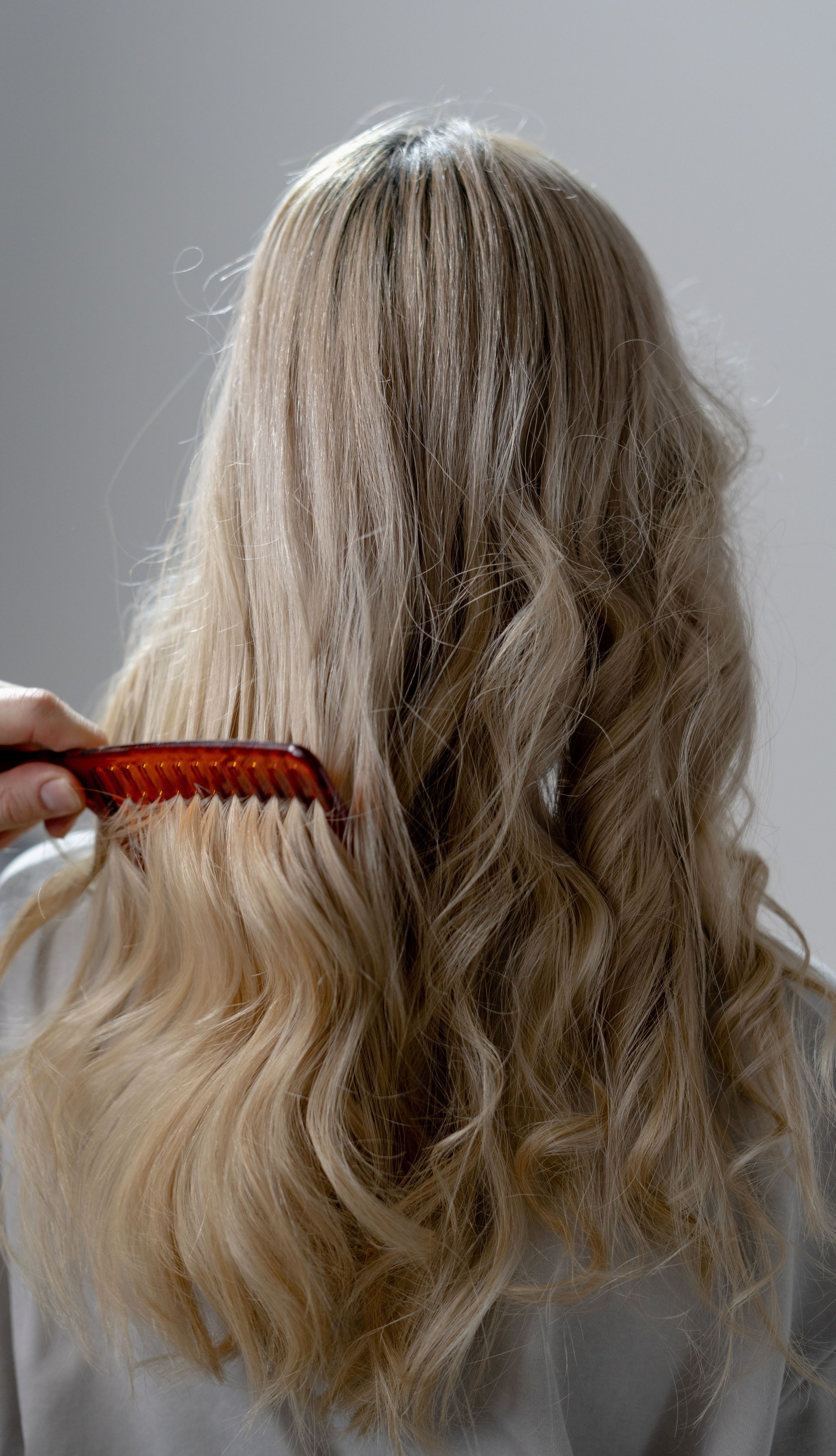 A woman with long wavy blonde hair is wearing a grey shirt who has balayage hair.