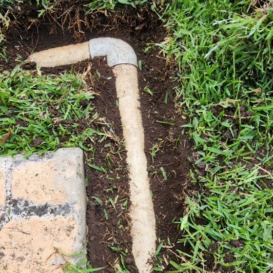 A Pipe is Laying in the Grass Next to a Brick — Dowds Pipe and Cable Locating in Farmborough Heights, NSW