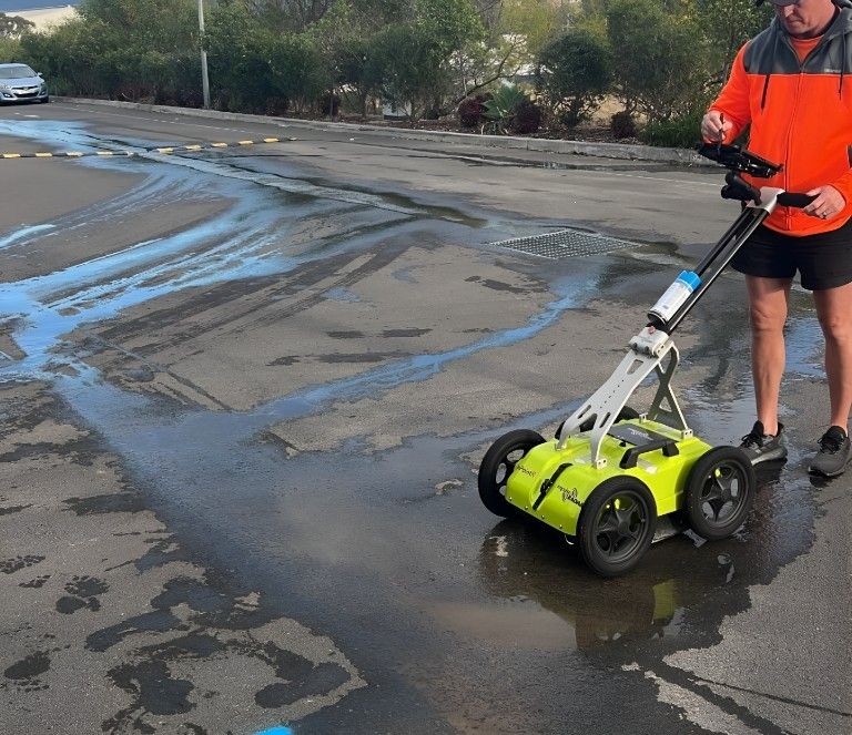 A Man in a Jacket is Using a Green Radar on a Wet Road — Dowds Pipe and Cable Locating in Sydney, NSW