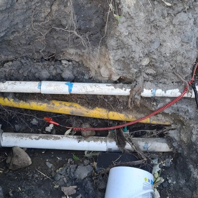 A Bucket is Sitting Next to a Bunch of Pipes in the Dirt — Dowds Pipe and Cable Locating in  Bowral, NSW