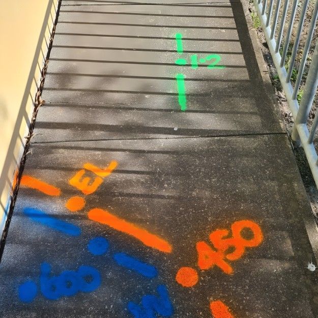 A Concrete Walkway Has a Green Cross Painted on It — Dowds Pipe and Cable Locating in Bondi, NSW