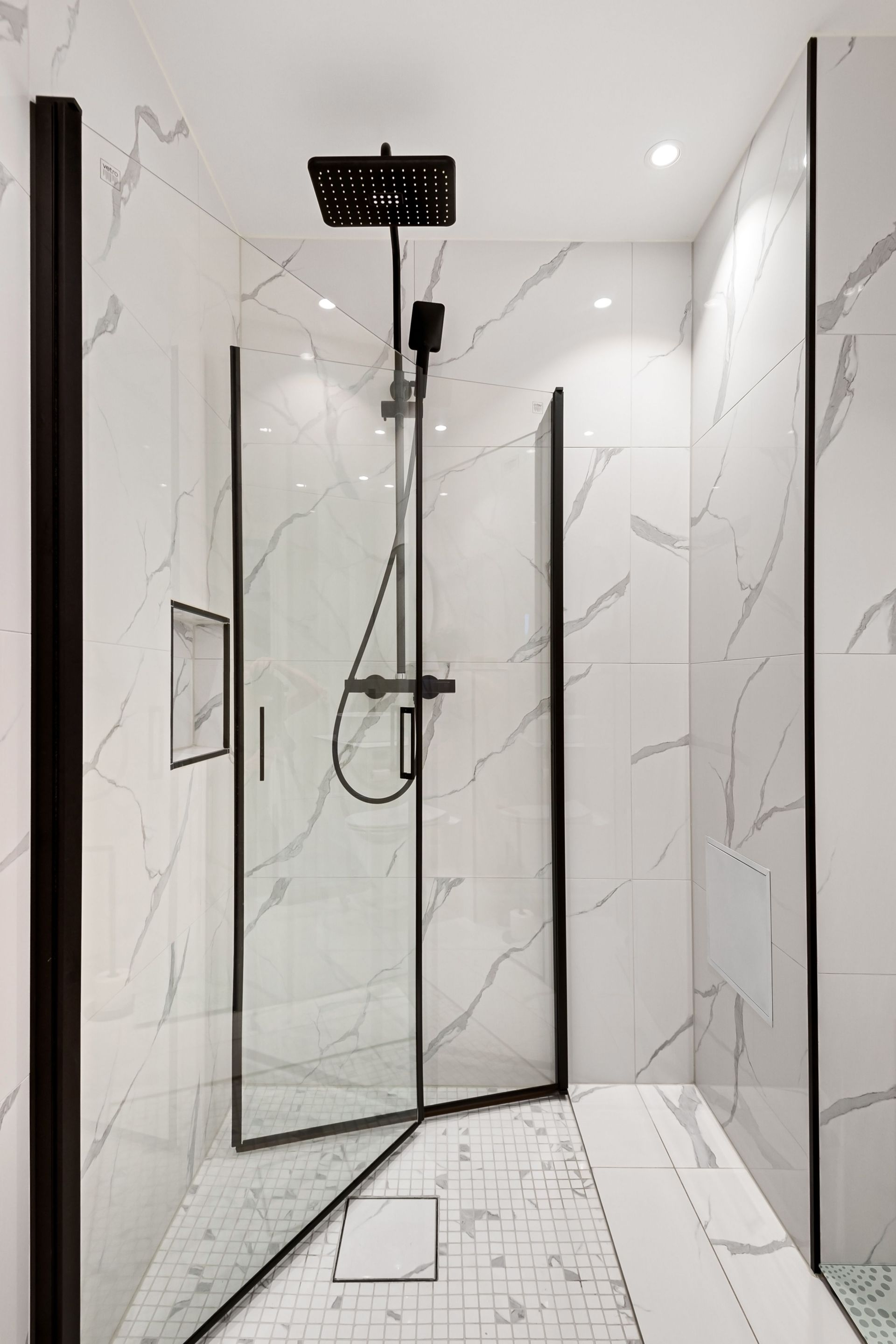 Modern marble-tiled shower with black fixtures, glass door, and rainfall showerhead