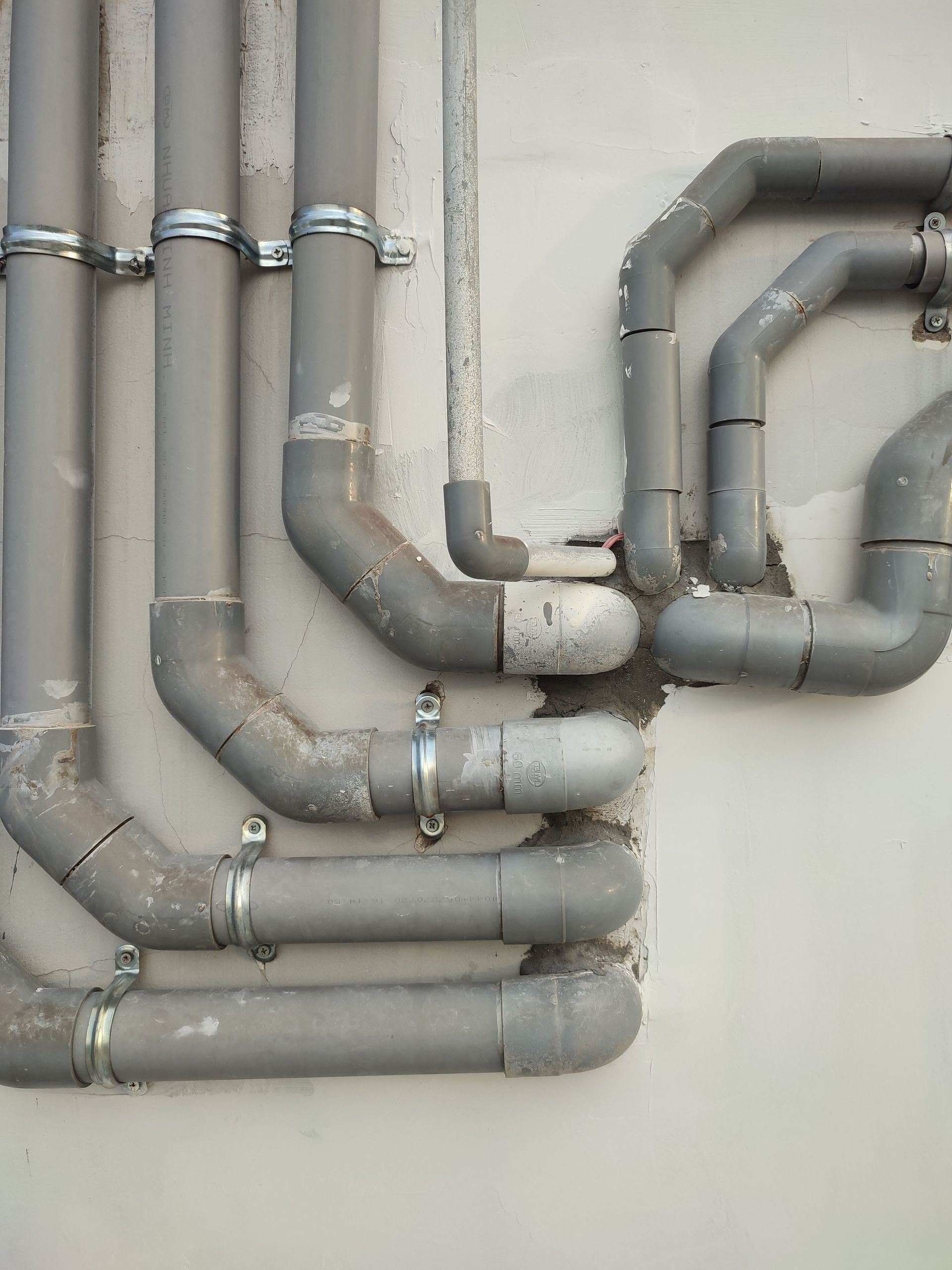 Gray pipes with metal clamps running along a wall and bending into multiple joints.