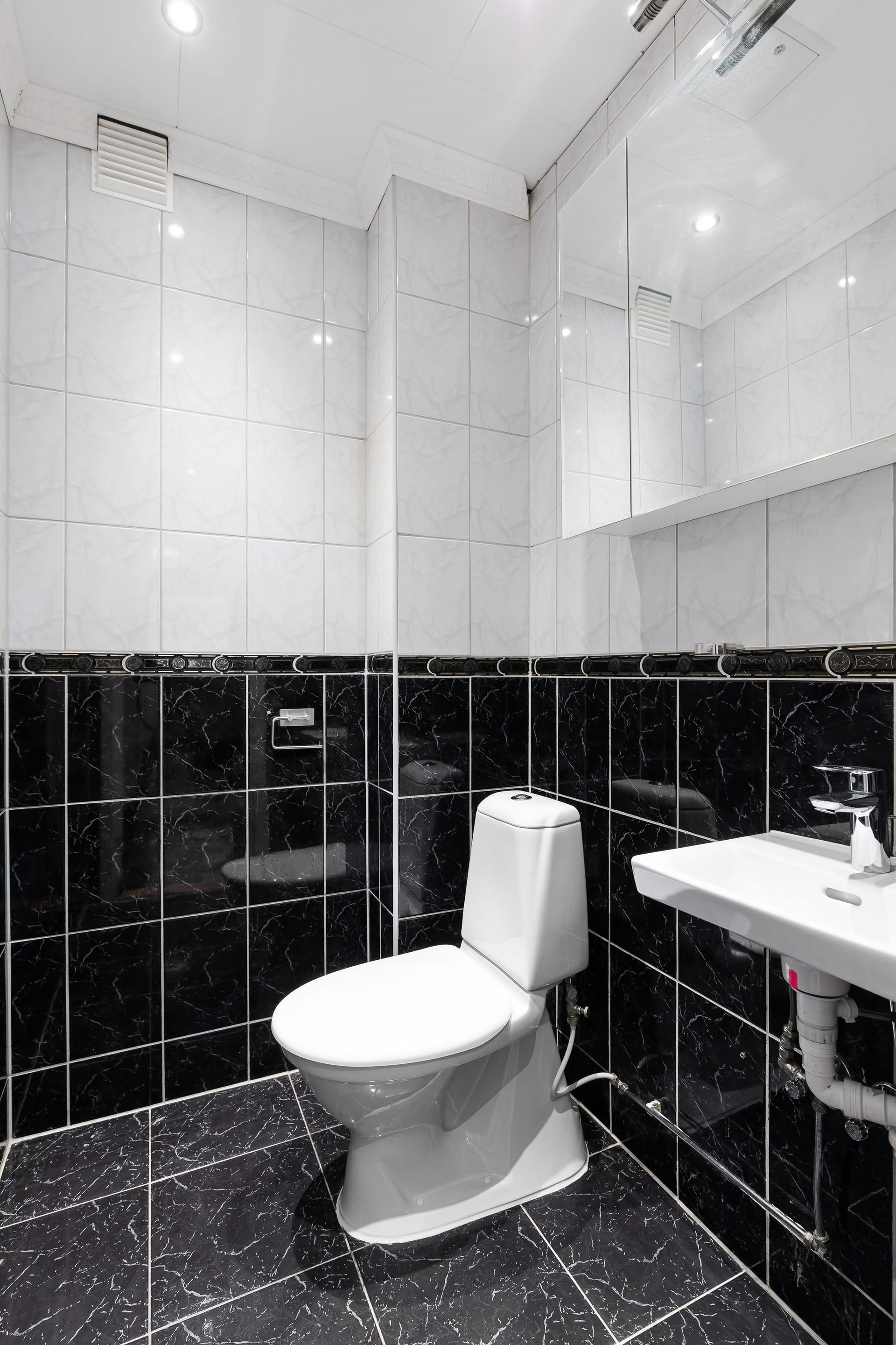 Small bathroom with black-and-white tiled walls, a toilet, sink, and wall cabinet.
