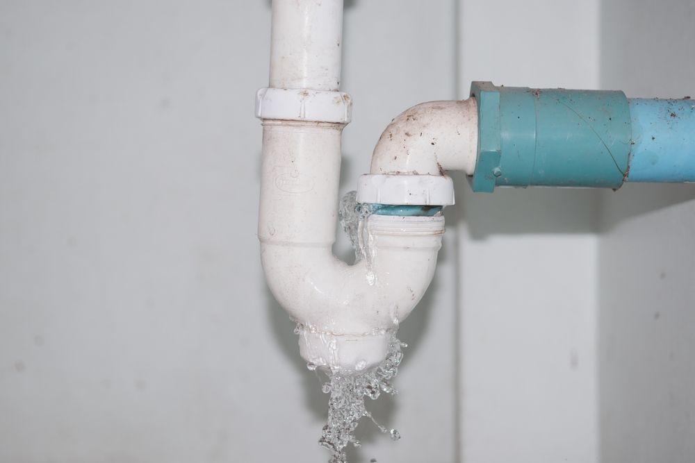 Leaking white PVC pipe joint with water dripping onto a wall.