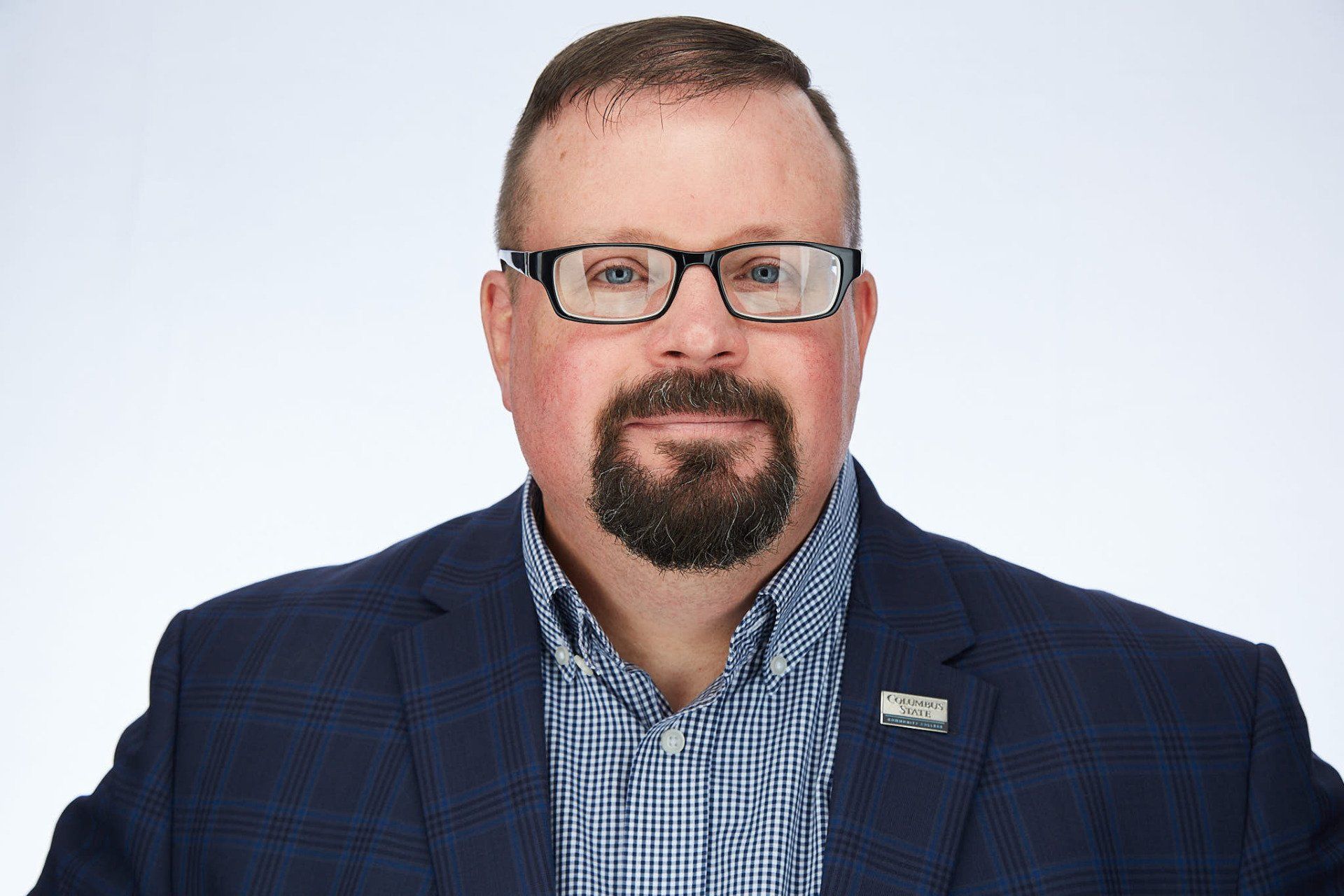 A man with a beard and glasses is wearing a suit and a plaid shirt.