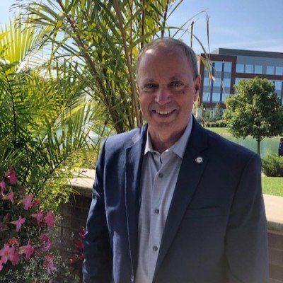 A man in a suit is smiling in front of a building
