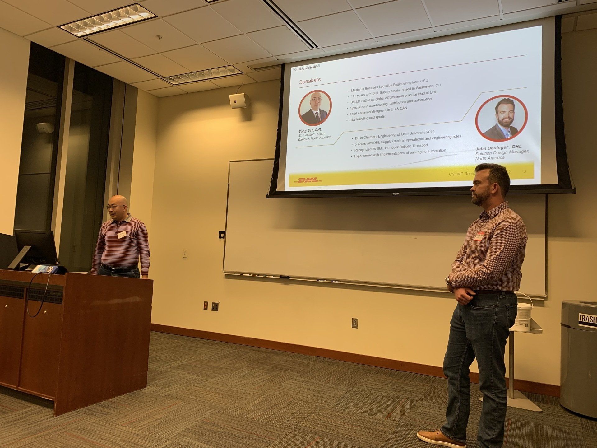 Two men are giving a presentation in front of a large screen.