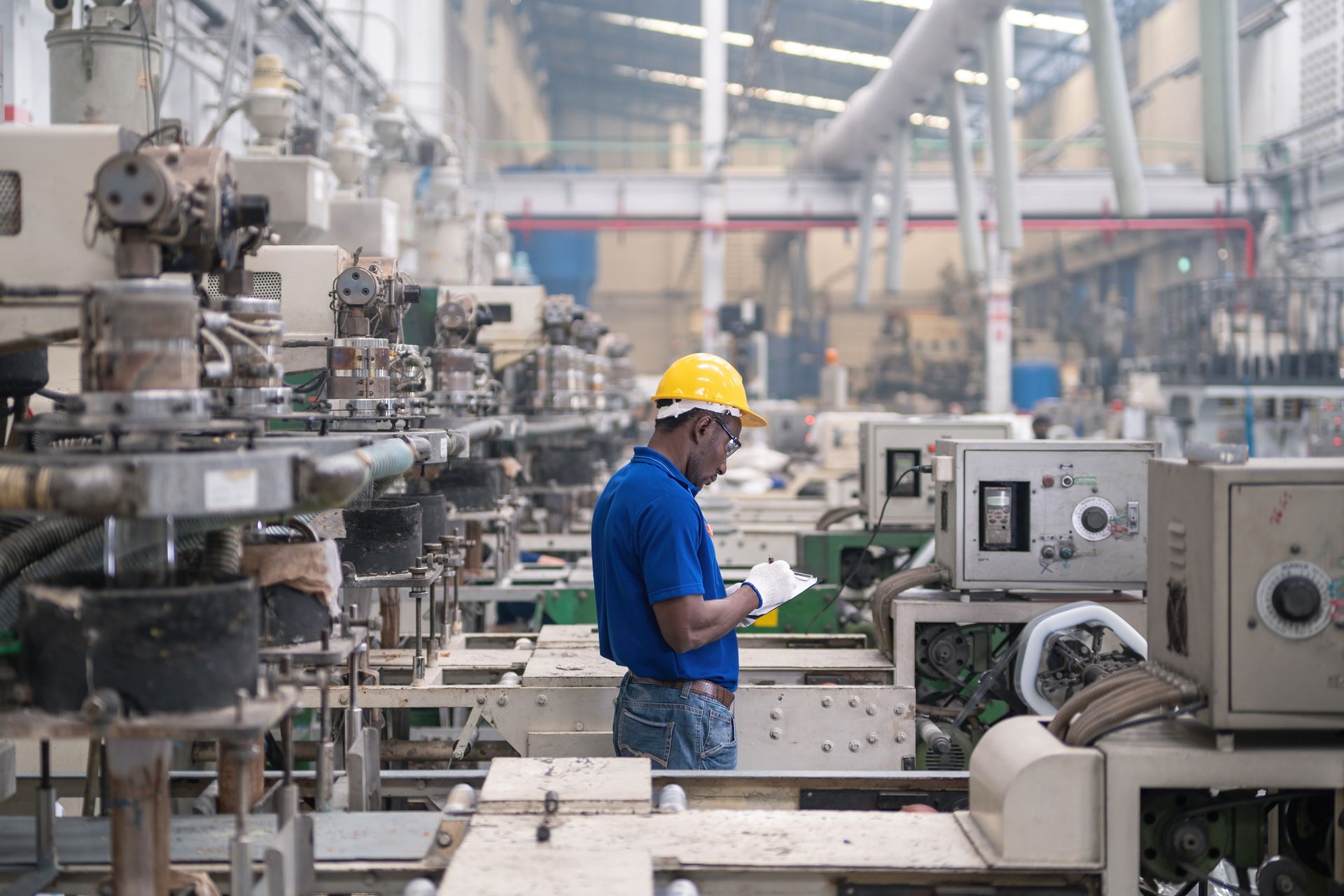 Worker in yellow hard hat inspecting machinery on a factory floor