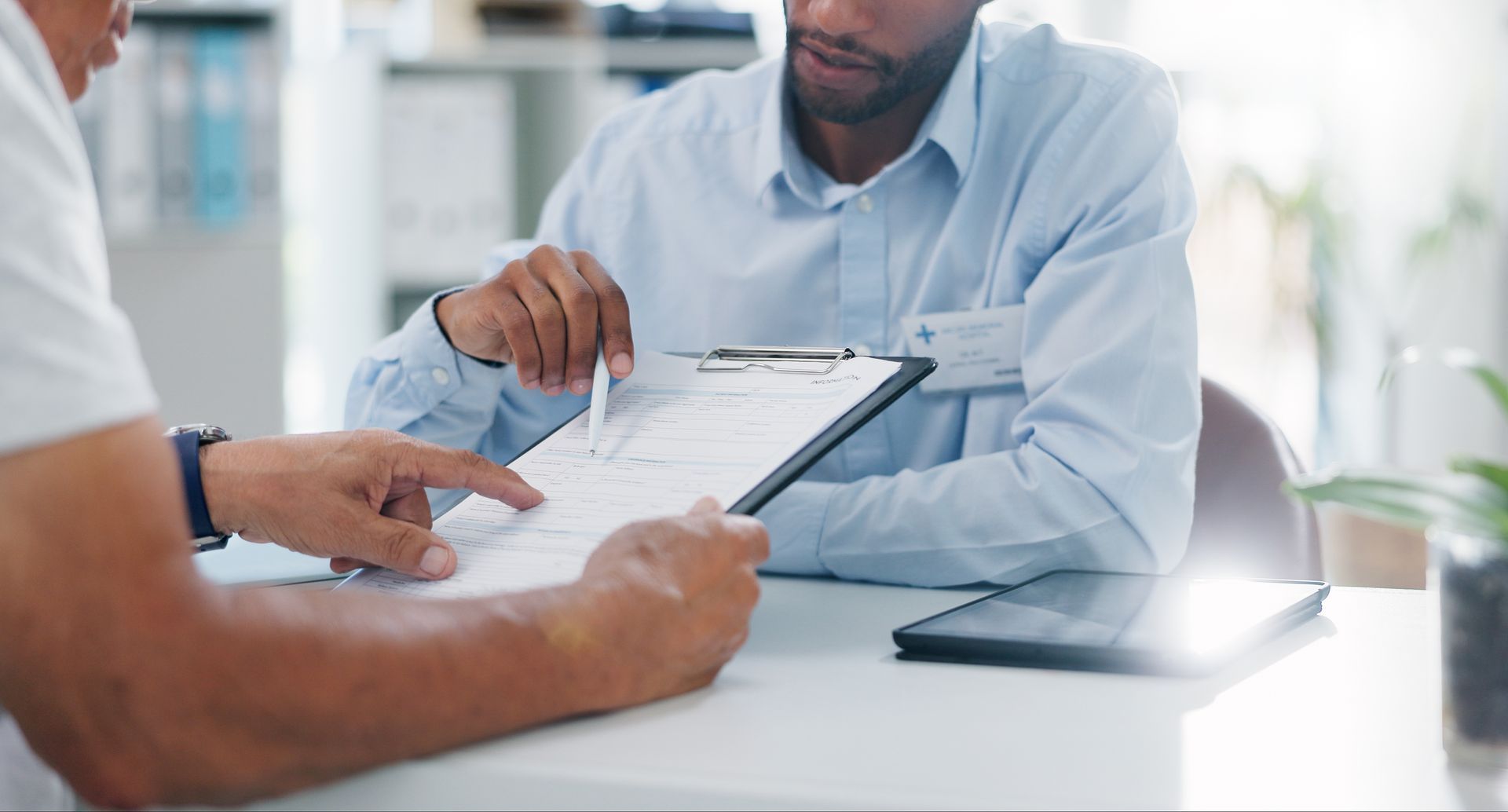 Two men in an office review a document on a clipboard. One points at the paper.