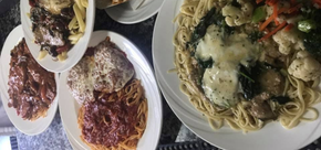 Plates of pasta with red sauce and a large bowl of creamy noodle soup on a table