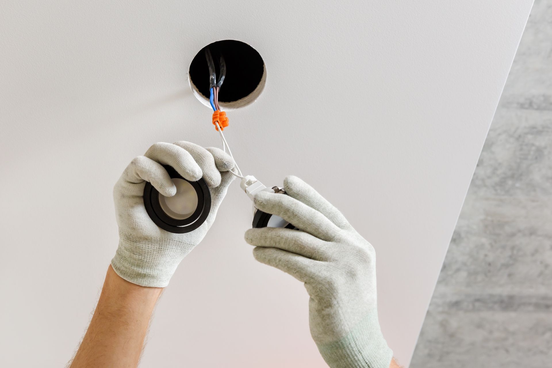 Person in gloves wiring ceiling light. Wires emerge from hole.