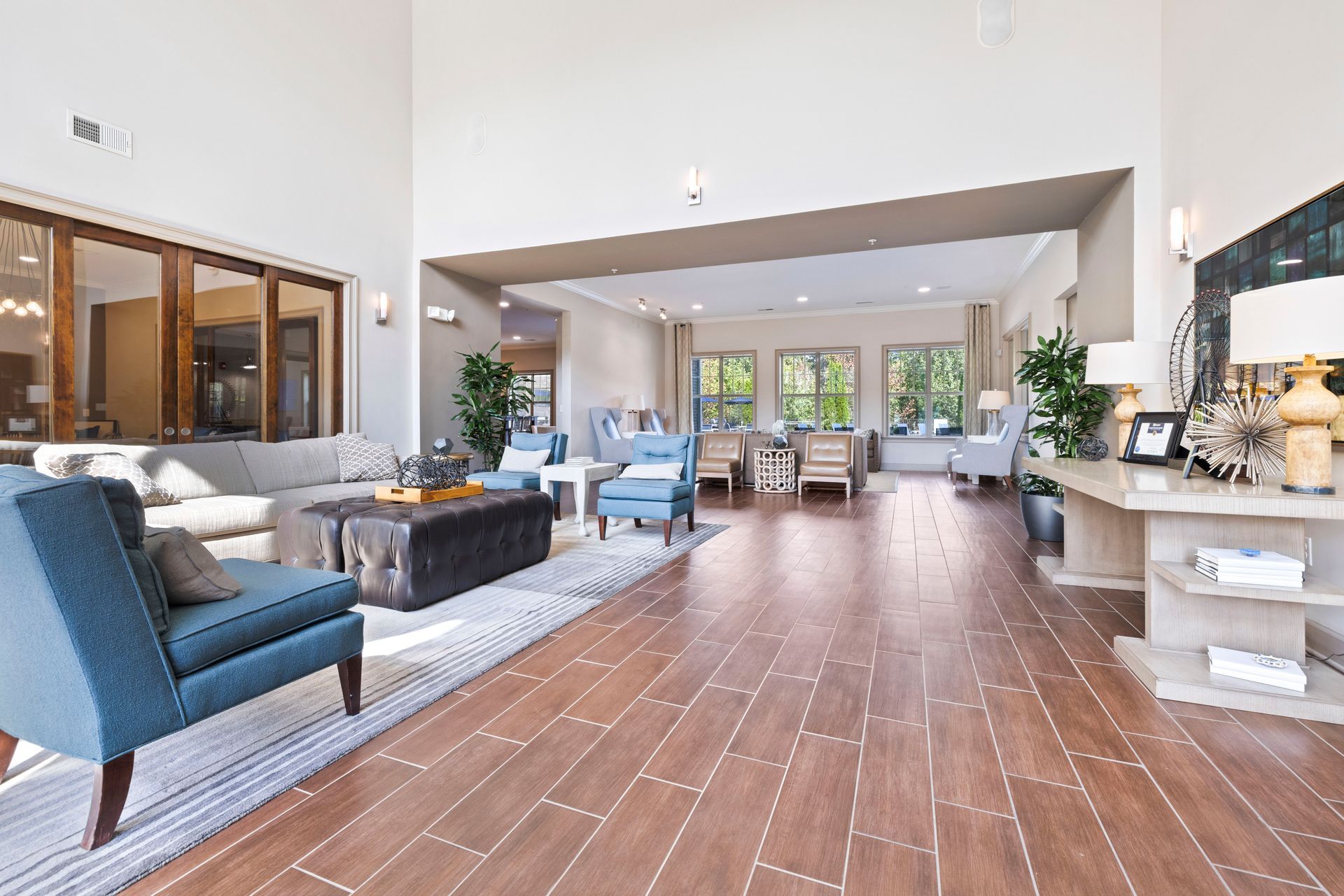 A bright, spacious open-concept lobby with blue armchairs, a large ottoman, and a side table on wood-look tile floors at Silver Collection at Waterford in Huntersville, NC.