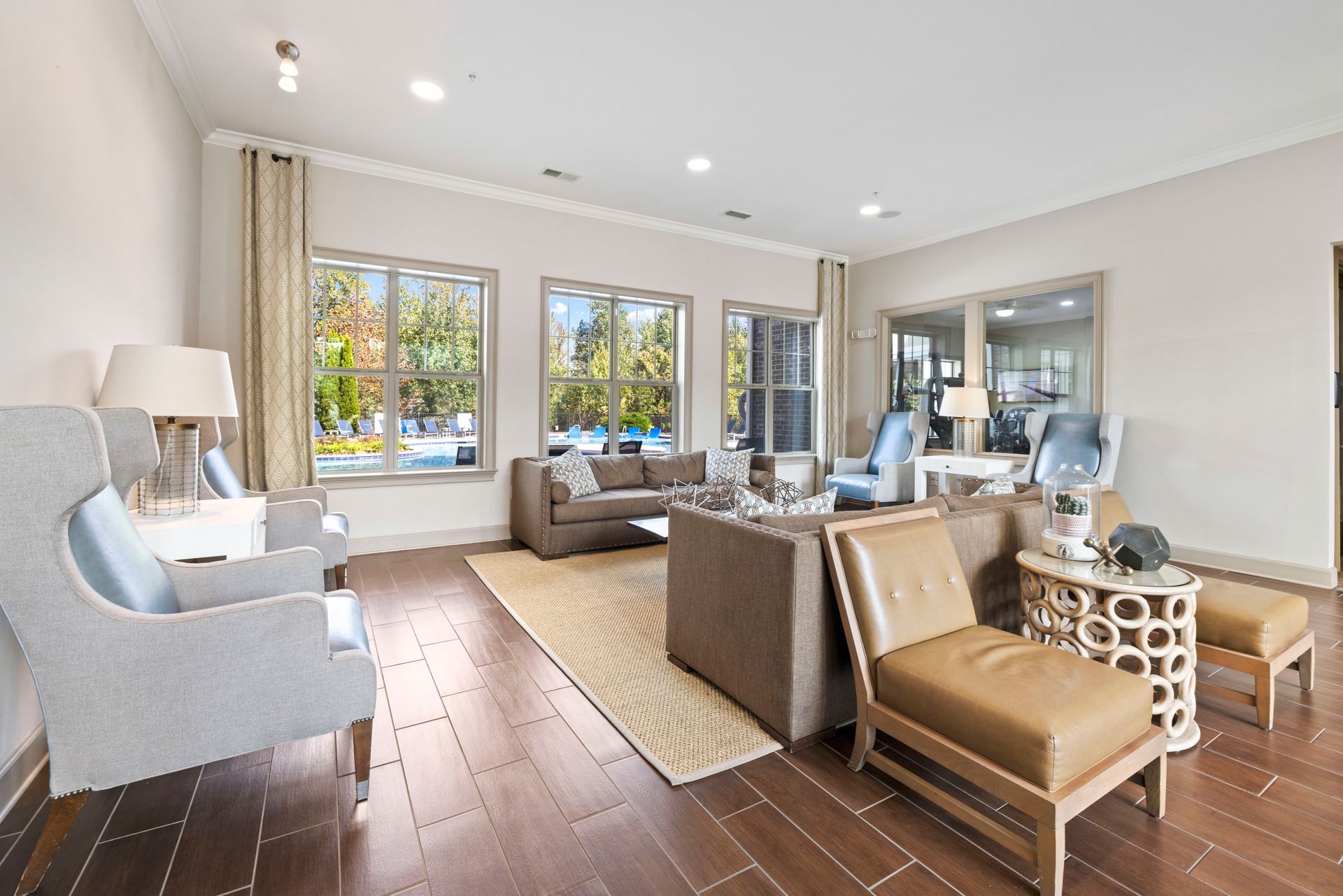 A spacious lobby with modern grey chairs, a brown sofa, a tan armchair, and windows overlooking a swimming pool at Silver Collection at Waterford in Huntersville, NC.