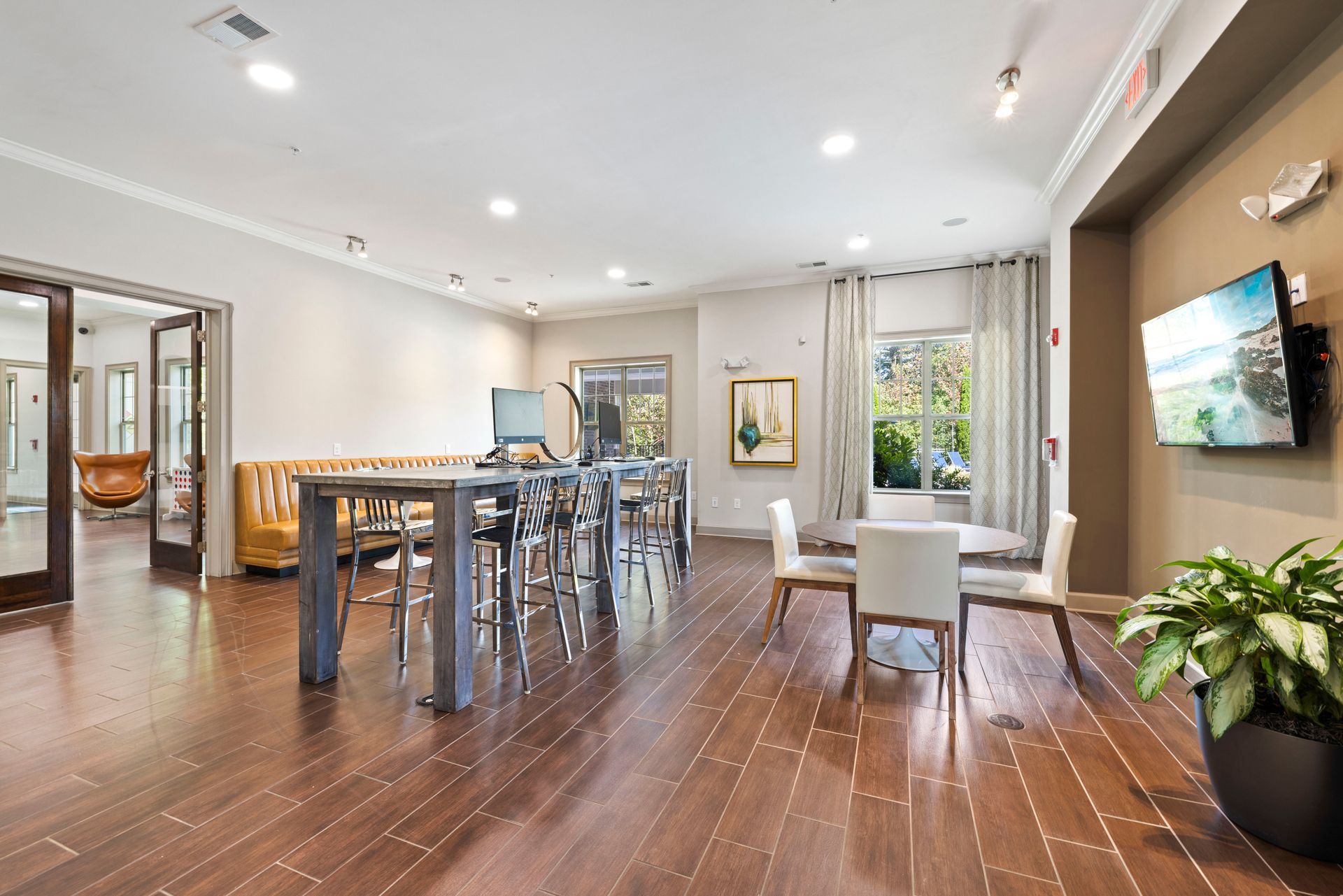 A bright, spacious common room with a long table, dining area, dark wood floors, and a wall-mounted TV at Silver Collection at Waterford in Huntersville, NC.