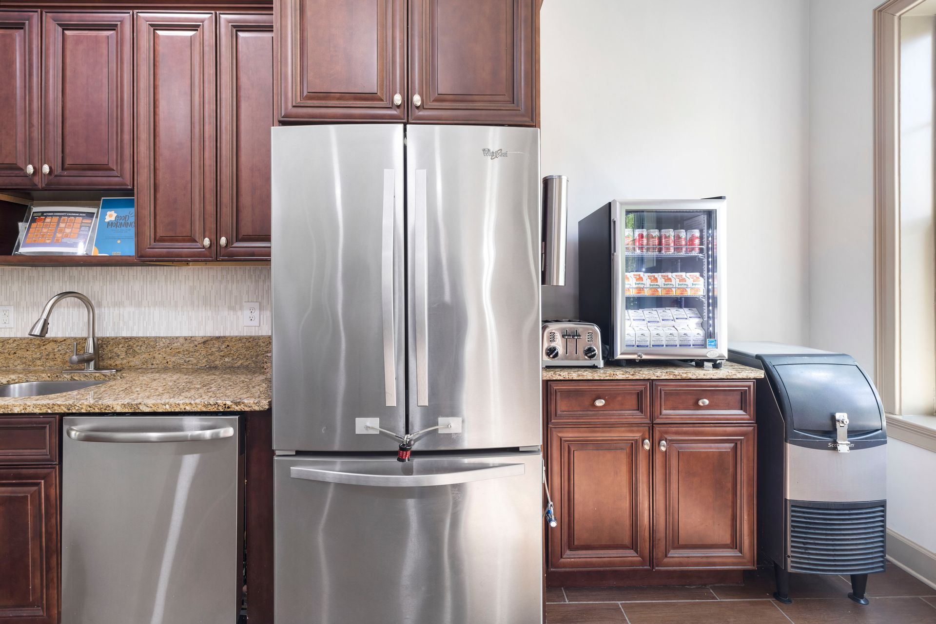 A kitchen featuring a stainless-steel refrigerator, dishwasher, beverage cooler, and ice maker with dark wood cabinets at Silver Collection at Waterford in Huntersville, NC.