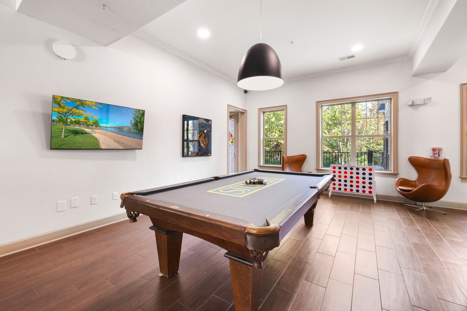 A game room featuring a wood-framed pool table, a wall-mounted TV displaying a landscape, and a leather egg-style chair at Silver Collection at Waterford in Huntersville, NC.