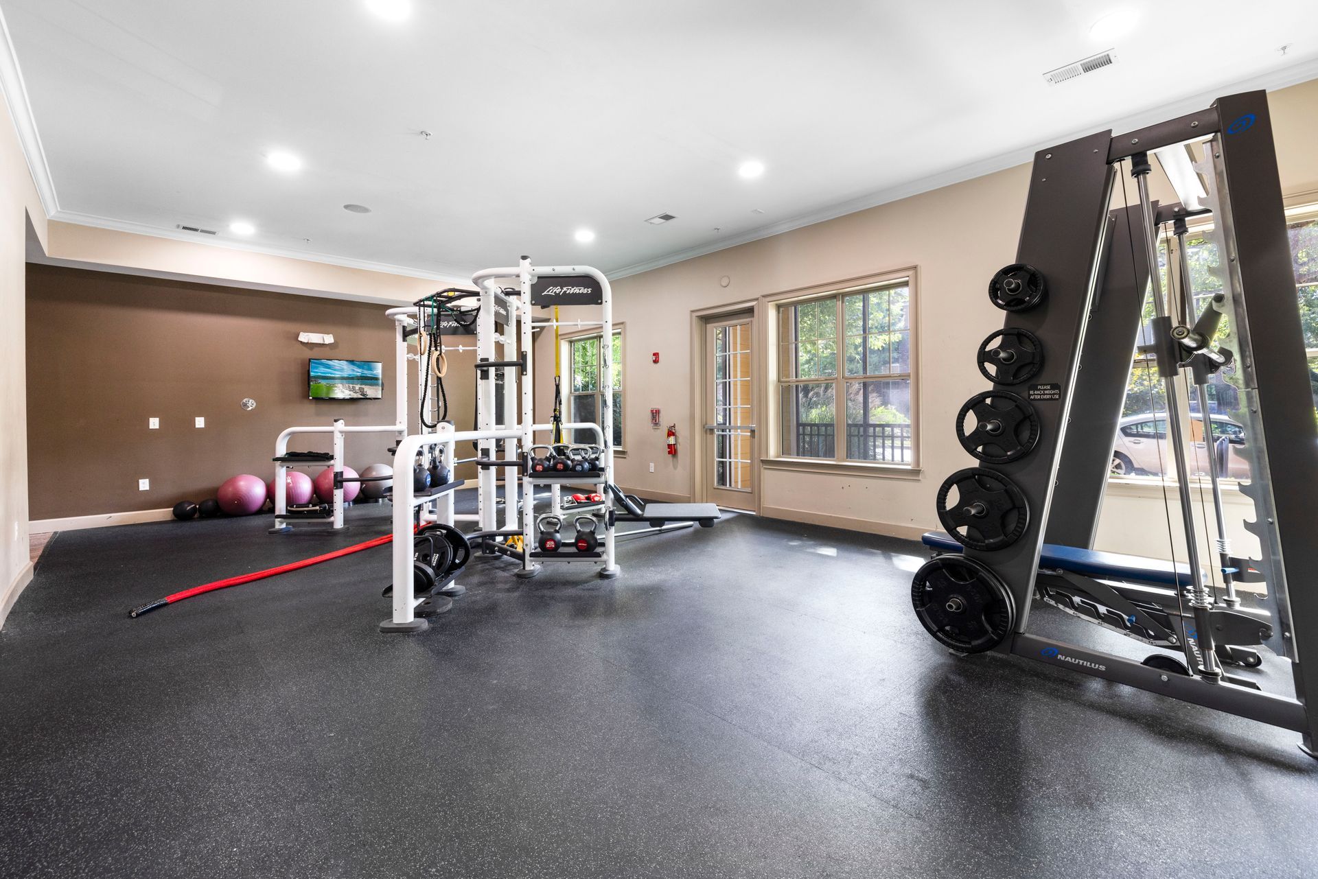 A fitness center featuring a weight rack, cable machine, and exercise balls on a black, speckled gym floor at Silver Collection at Waterford in Huntersville, NC.