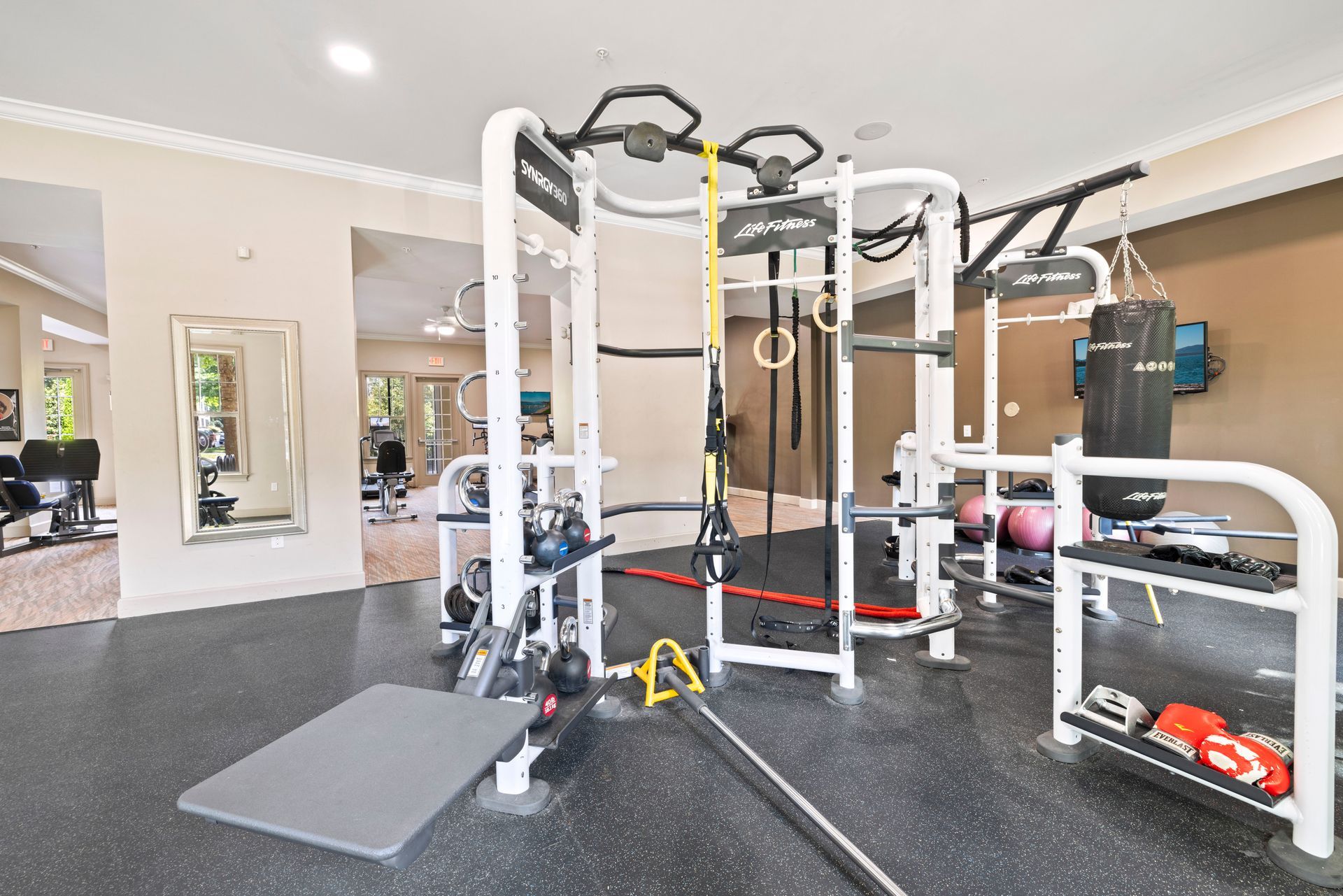 A gym room featuring a central multi-functional exercise rig, a punching bag, and weight storage shelves at Silver Collection at Waterford in Huntersville, NC.