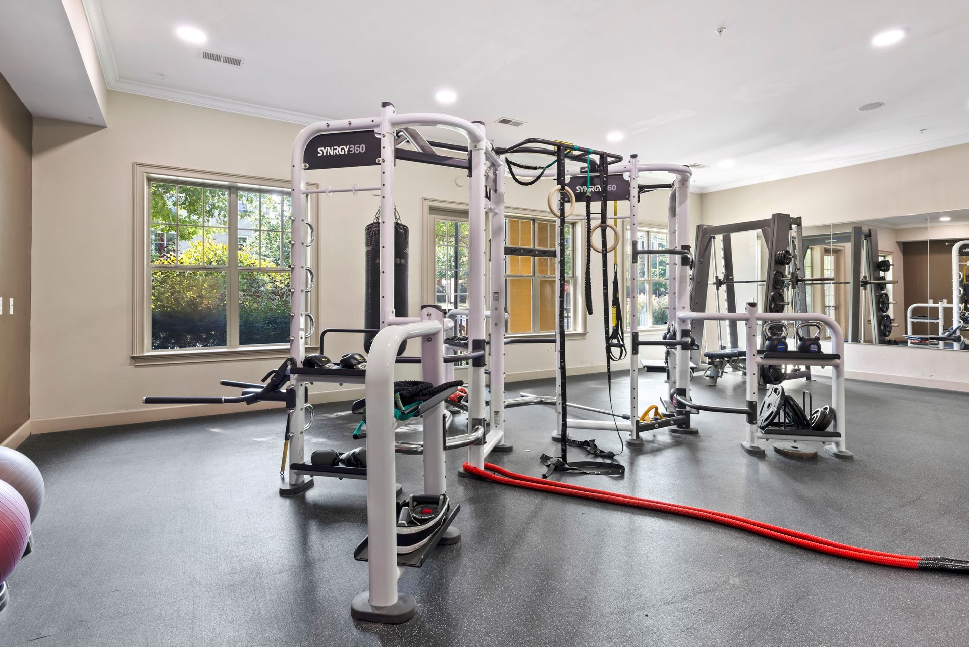 A brightly lit apartment fitness center featuring a white multi-station functional training rack and rubber flooring at Silver Collection at Waterford in Huntersville, NC.