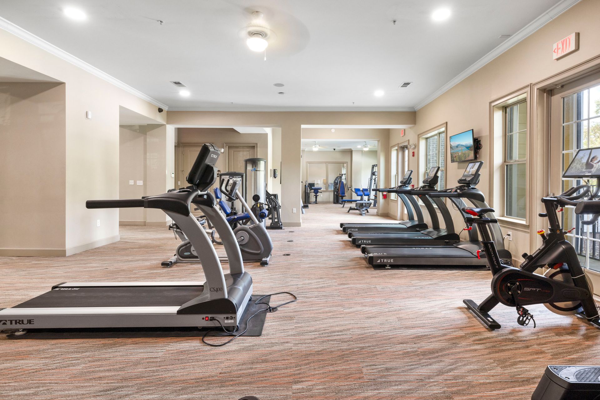 A brightly lit apartment gym with multiple treadmills and a stationary bike on a carpeted floor at Silver Collection at Waterford in Huntersville, NC.