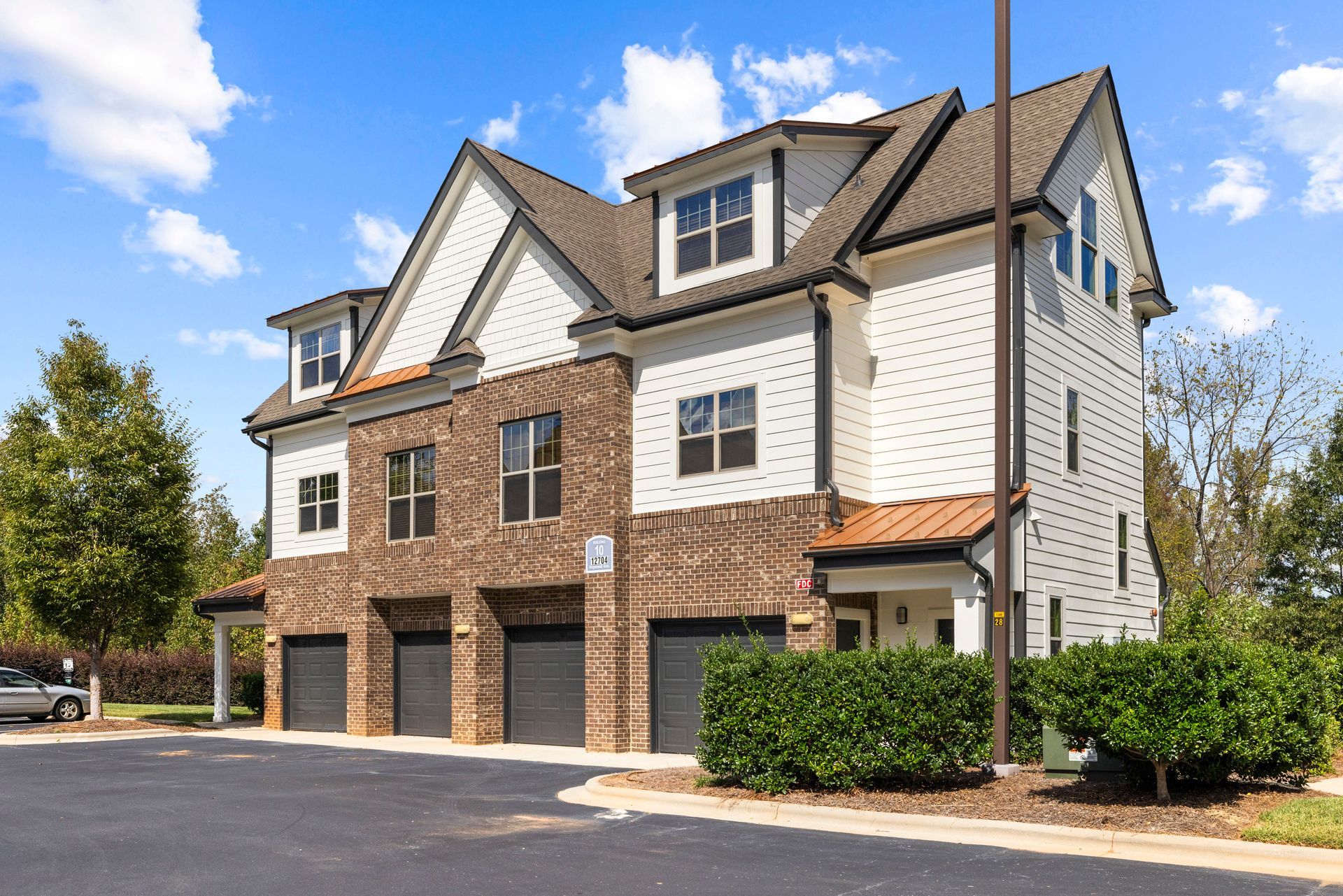 A three-story building with white siding and brown brick, featuring four garage doors at street level, under a blue sky at Silver Collection at Waterford in Huntersville, NC.