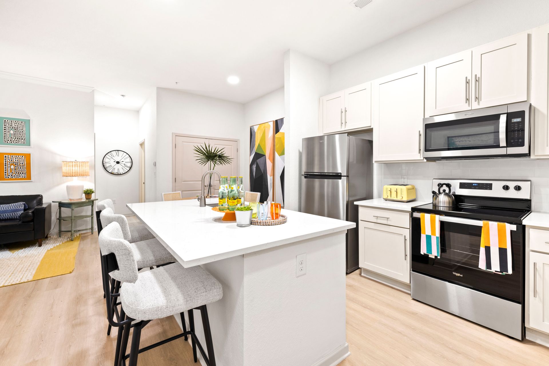 Modern apartment kitchen with a white island, stainless steel appliances, and wood-style flooring.