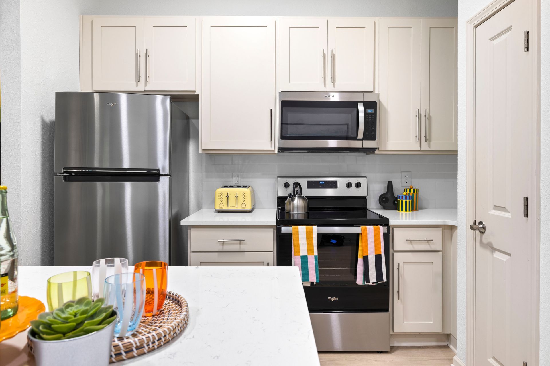 A modern kitchen with off-white cabinets, stainless steel appliances, and a white countertop in the foreground.