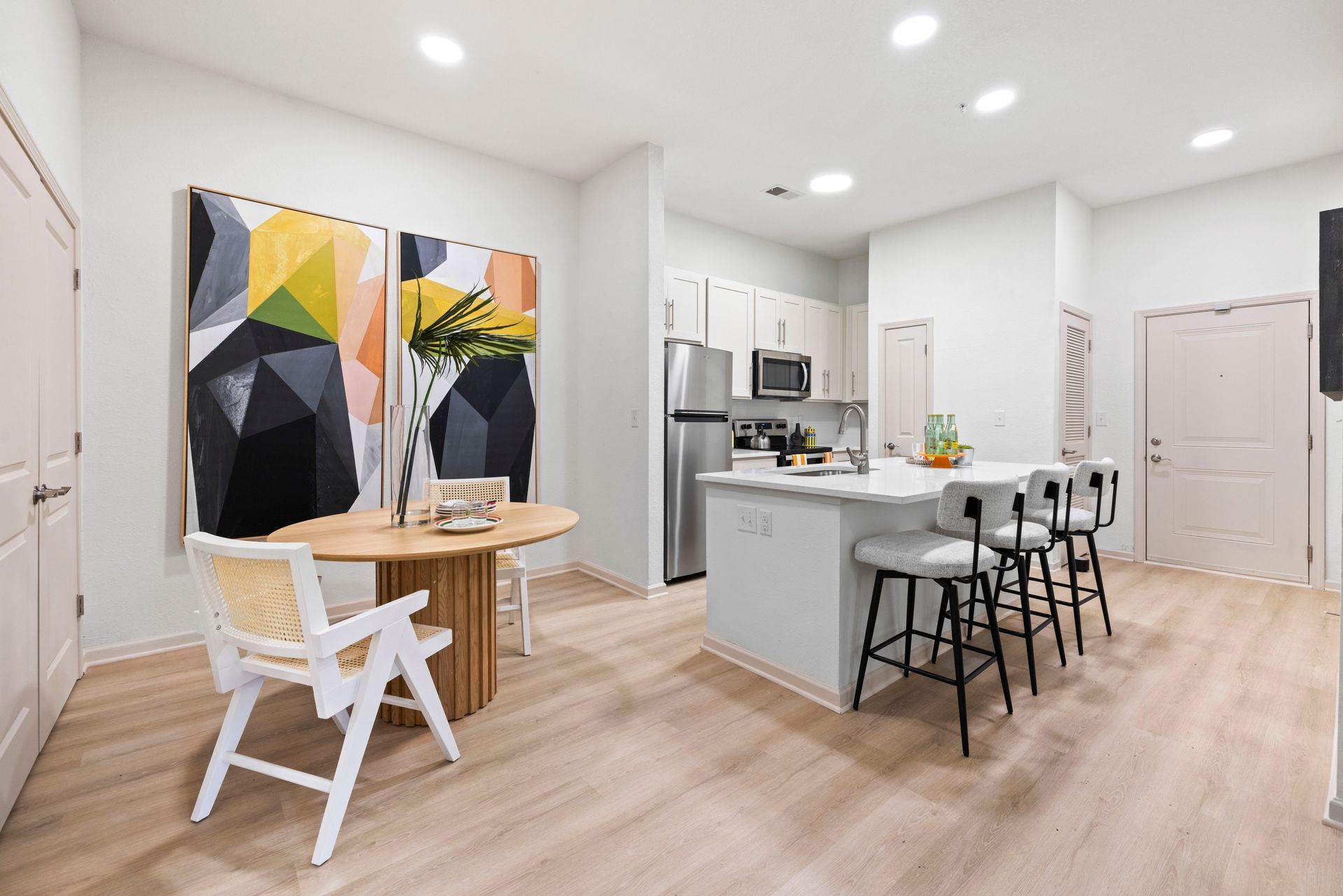 A modern kitchen and dining area with light wood floors, a circular table, and a kitchen island with stools.