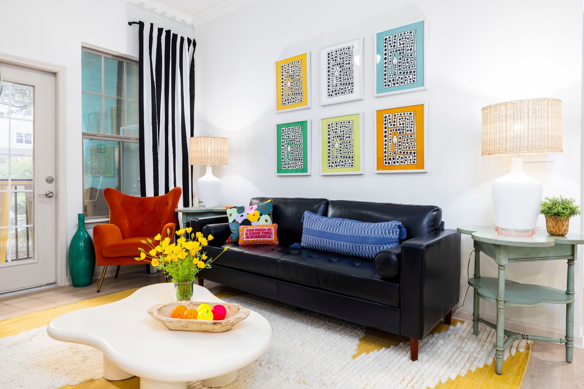 A colorful living room with a black sofa, orange armchair, abstract wall art, and an organic-shaped white coffee table at Silver Collection at Waterford in Huntersville, NC.