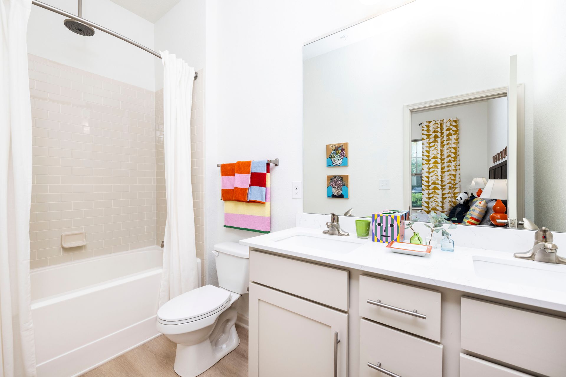 A modern, bright bathroom with a white vanity, a large mirror, a toilet, and a bathtub with a white shower curtain.