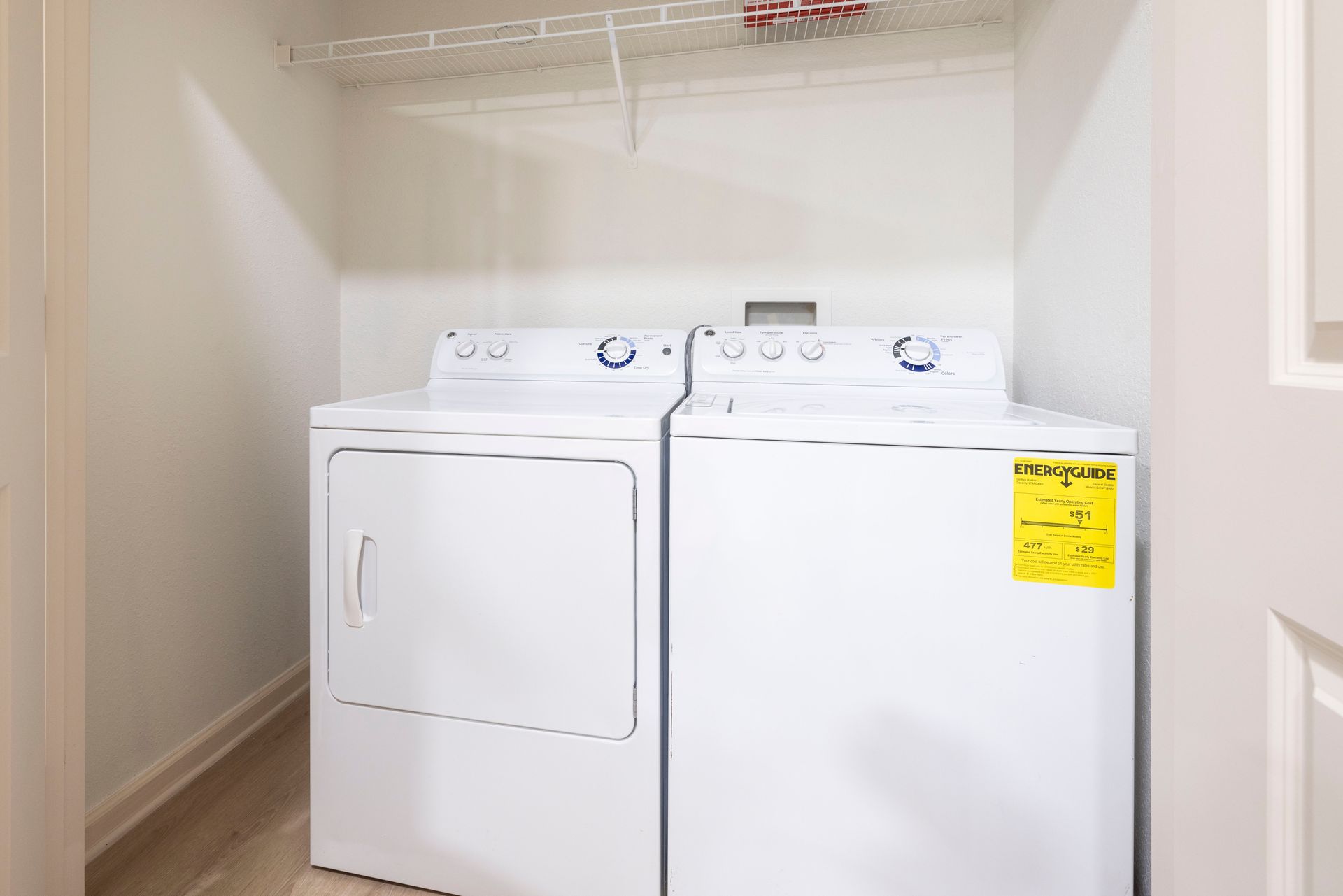 White clothes washer and dryer set sitting side-by-side in a small closet with an overhead wire storage shelf at Silver Collection at Waterford in Huntersville, NC.