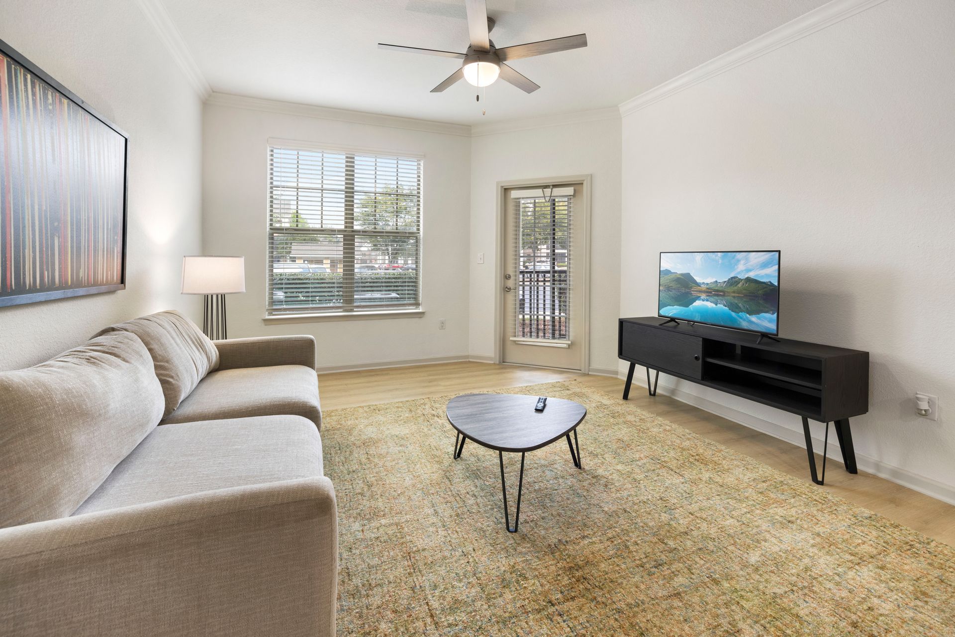 A light-filled living room featuring a tan sofa, a glass-topped coffee table, and a TV on a dark console at Silver Collection at Waterford in Huntersville, NC.