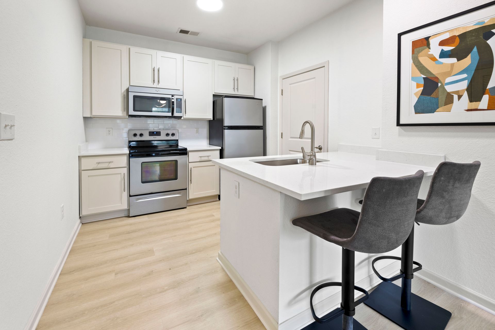 A modern kitchen featuring white cabinets, stainless steel appliances, a light-colored island with two grey bar stools at Silver Collection at Waterford in Huntersville, NC.