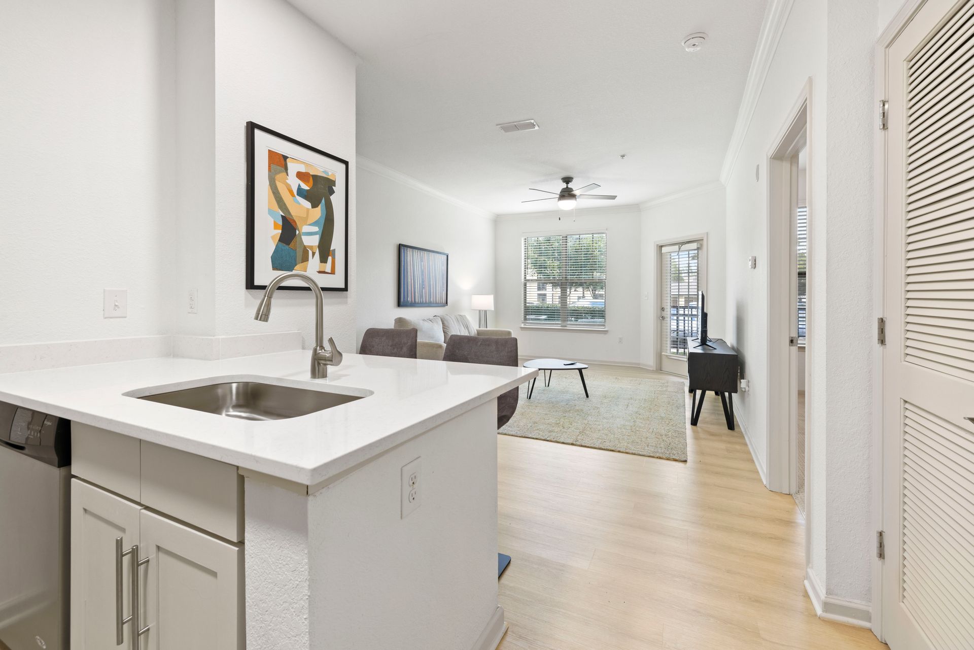 A kitchen island with a sink in the foreground opens into a bright living room with neutral furniture and wood floors at Silver Collection at Waterford in Huntersville, NC.