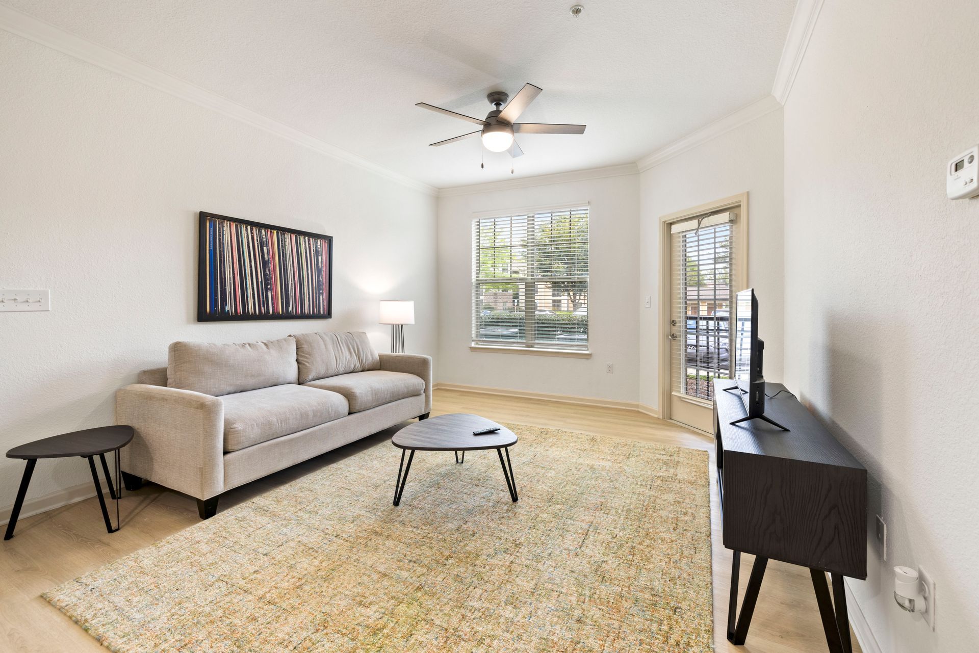 A bright living room features a beige sofa, two small black coffee tables, a textured rug, and a television on a stand at Silver Collection at Waterford in Huntersville, NC.