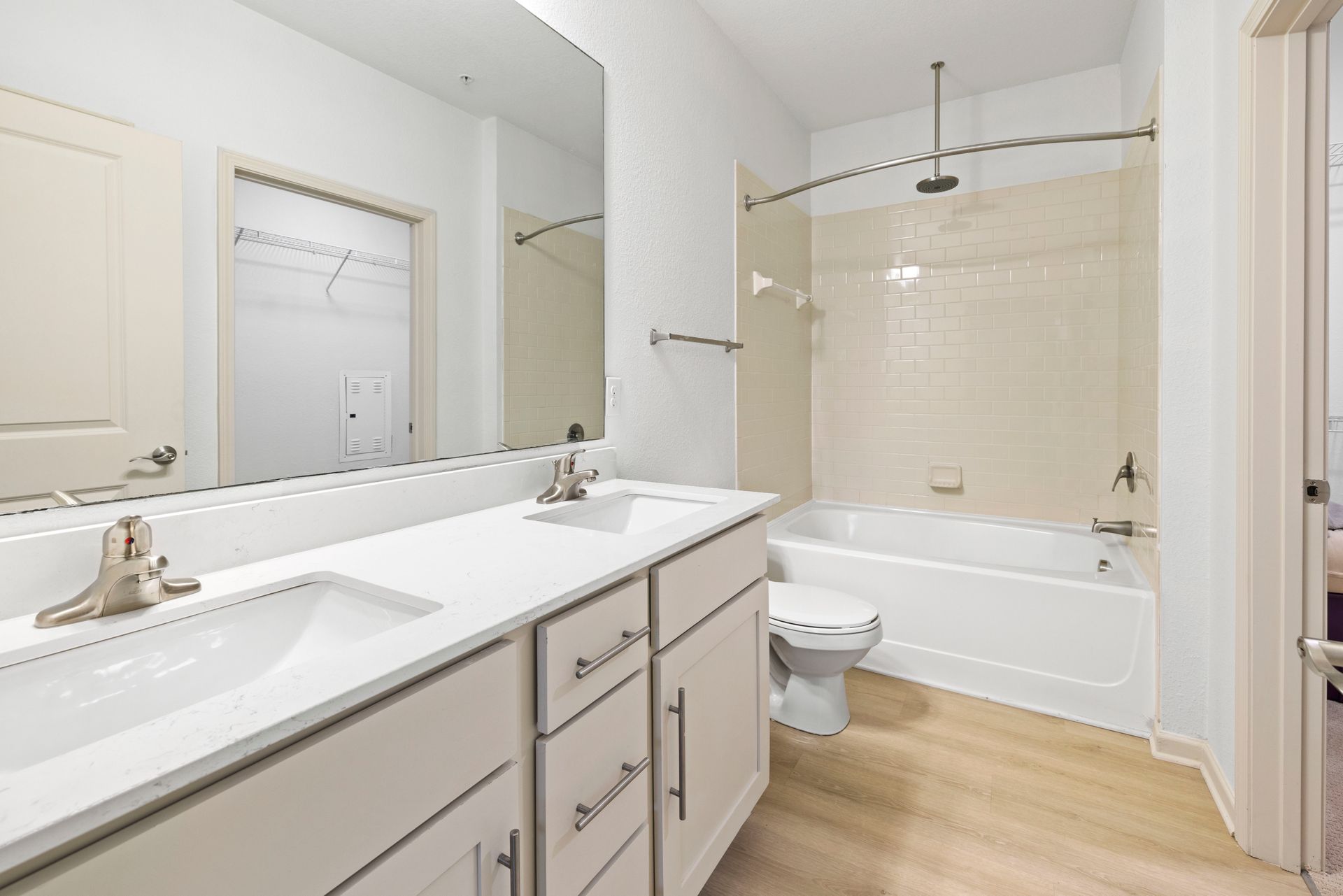 A bright, modern bathroom with white double vanities, a large mirror, a toilet, and a bathtub with a shower curtain rod at Silver Collection at Waterford in Huntersville, NC.