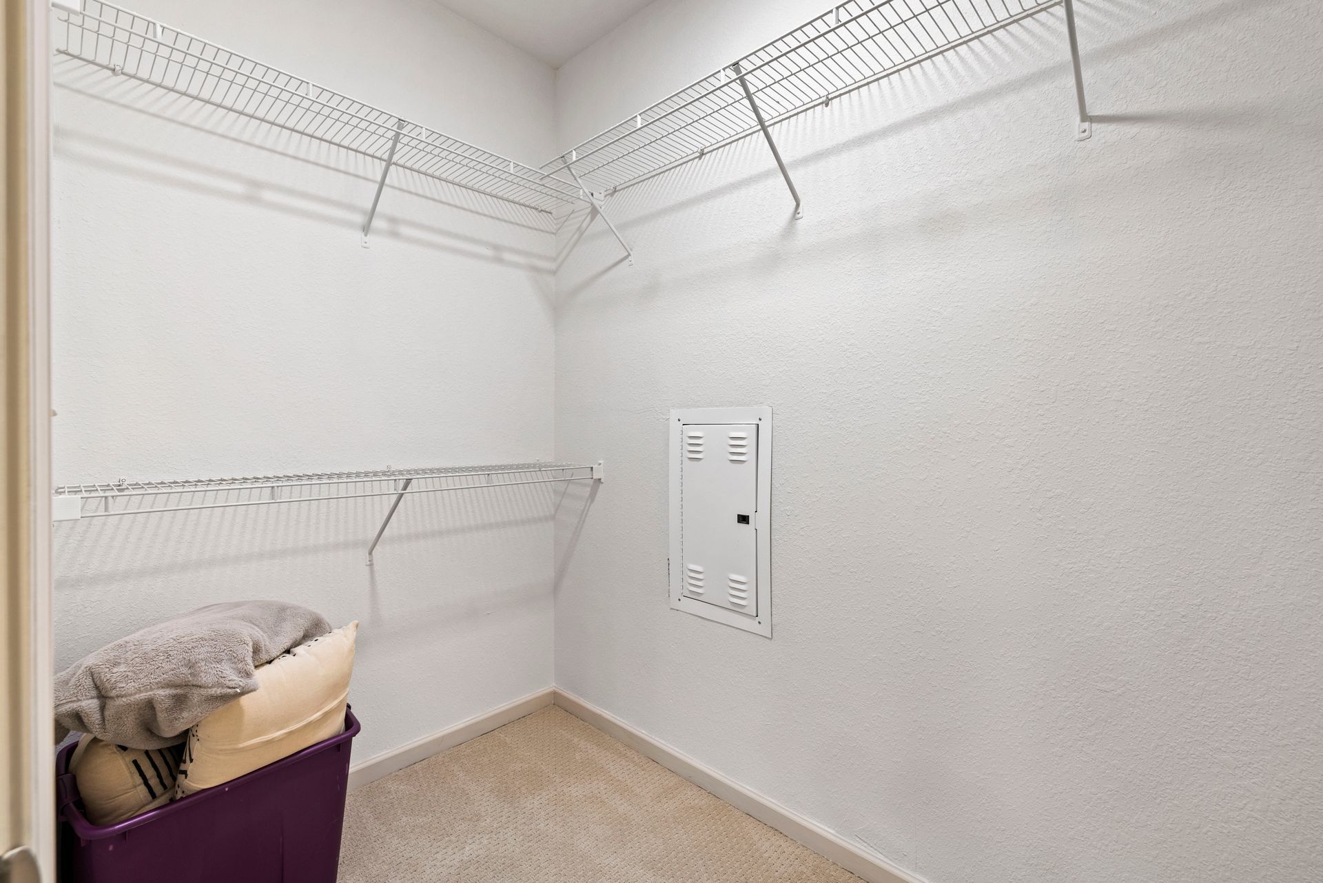 A walk-in closet with white walls, carpeted floor, white wire shelving, and an electrical panel mounted on the back wall at Silver Collection at Waterford in Huntersville, NC.