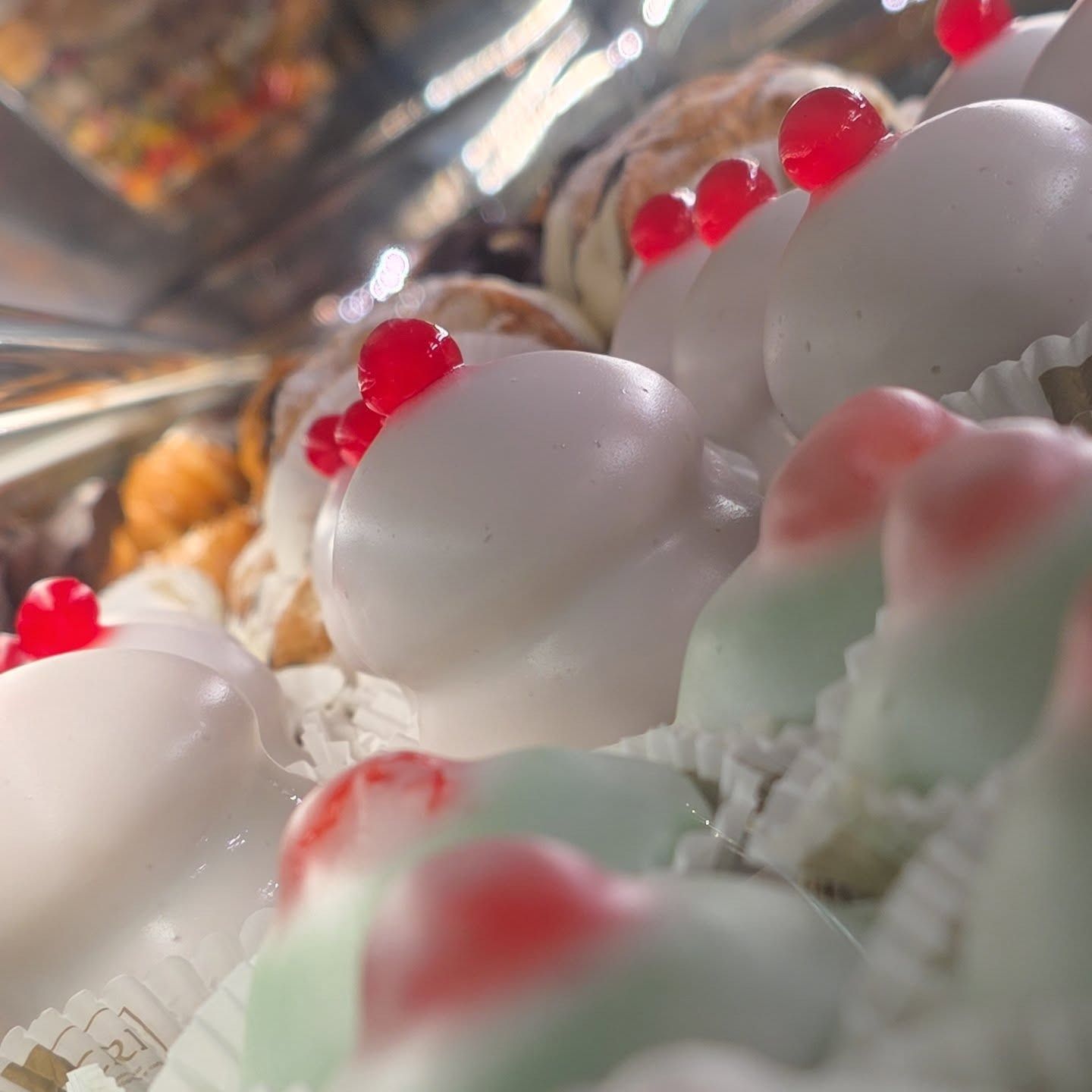 Pasticcini, glassa bianca con ciliegie rosse, esposti in una vetrina da pasticceria.
