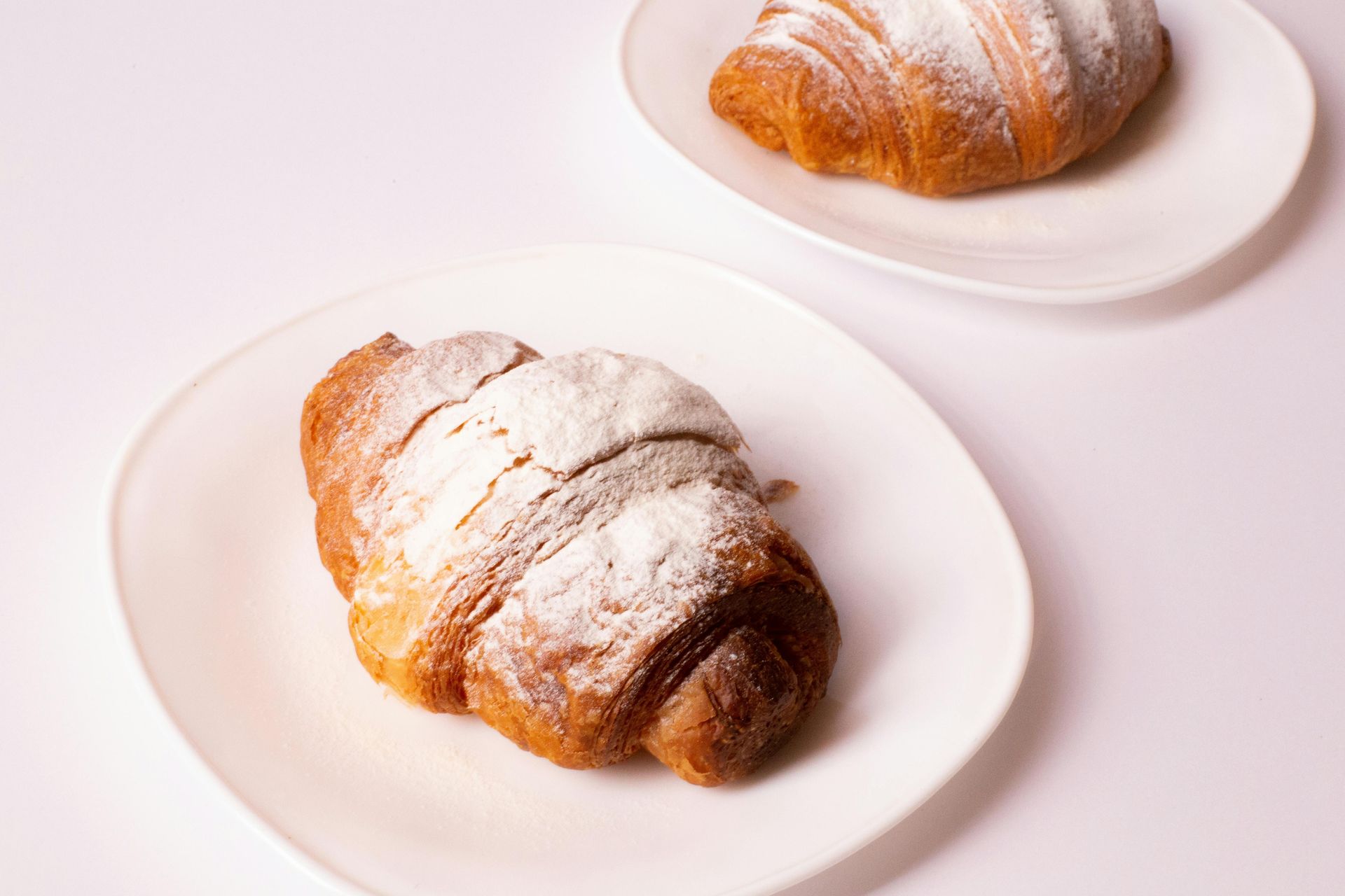 Due croissant spolverati con zucchero a velo su piatti bianchi.