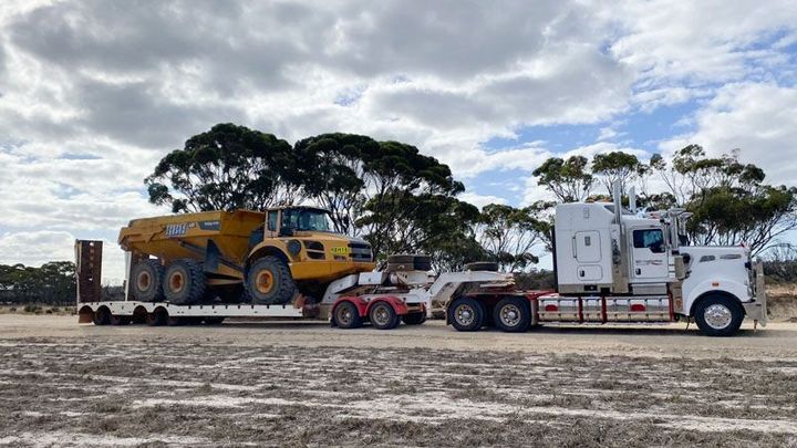 A semi truck is carrying a large excavator on a trailer.