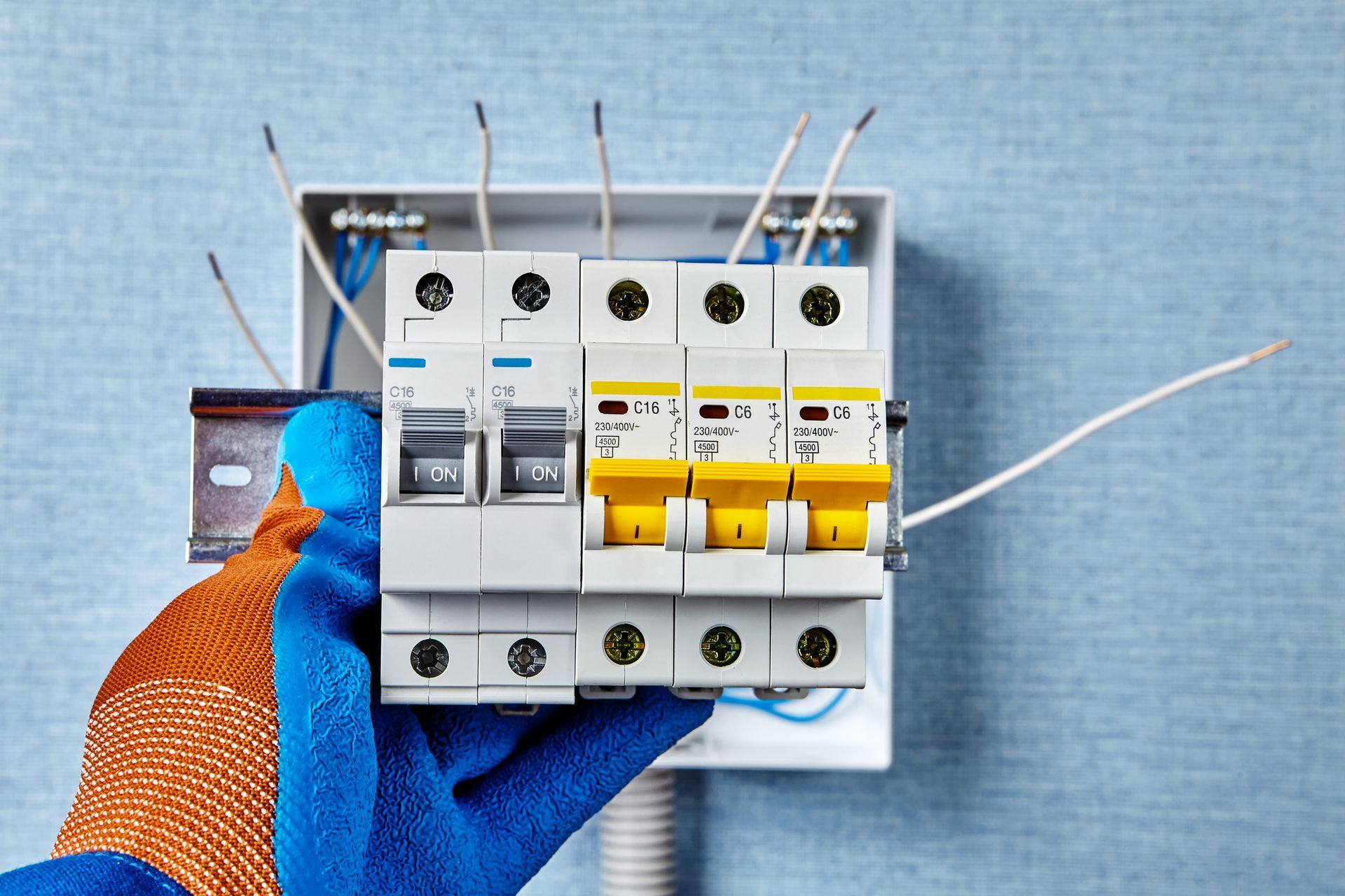 Hand holding electrical circuit breakers near a blue wall.