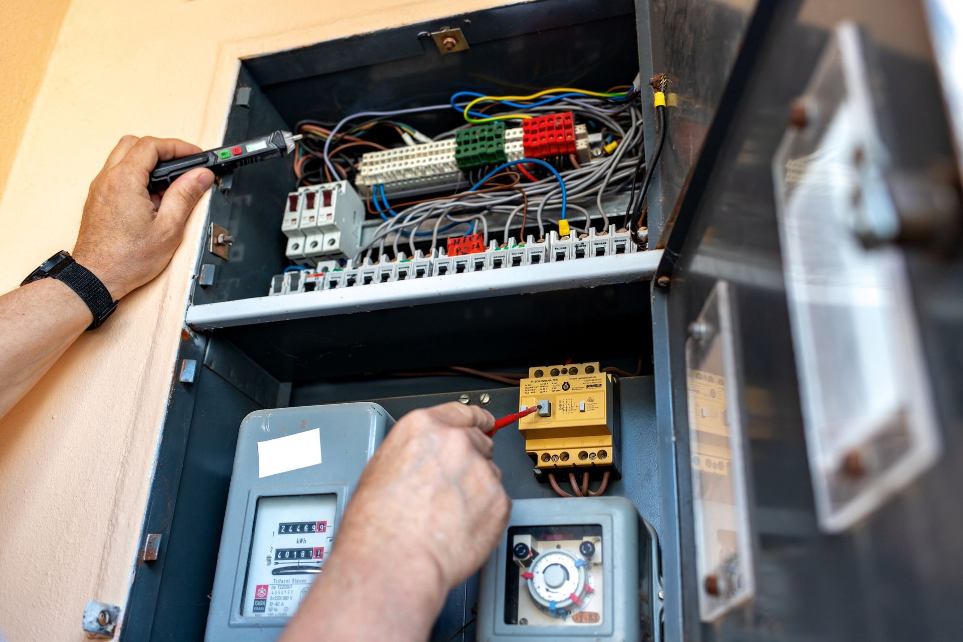 Electrician inspecting a circuit breaker box with a screwdriver and a testing device.