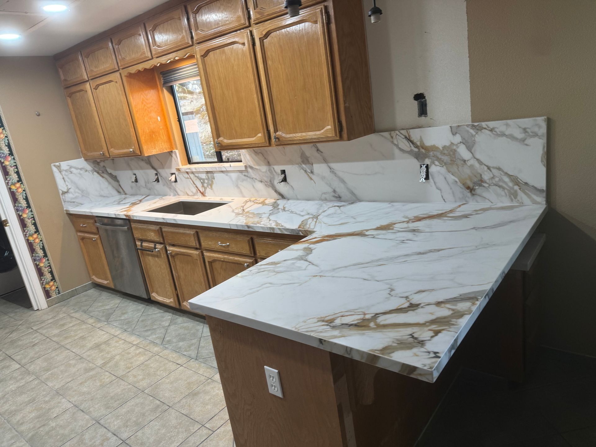 A kitchen features oak cabinets, stainless steel appliances, and white marble-look countertops and matching backsplash.