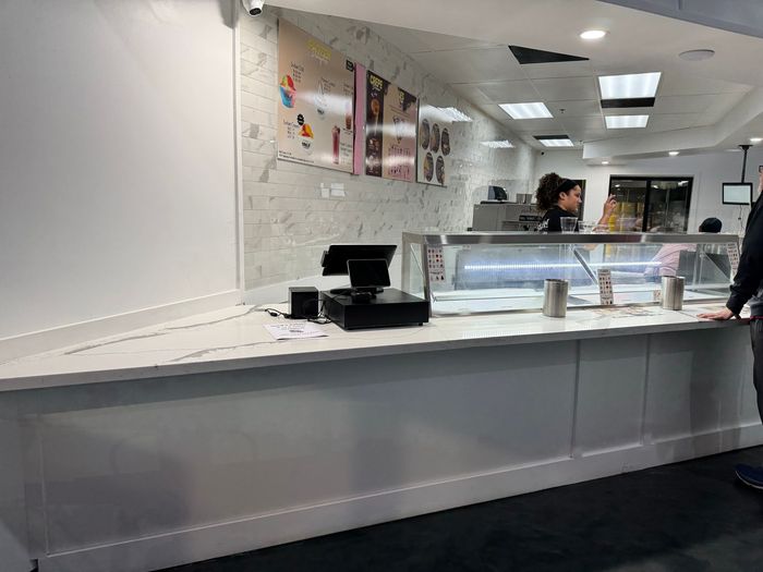 Bright restaurant counter with a glass display case and a staff member behind the register.