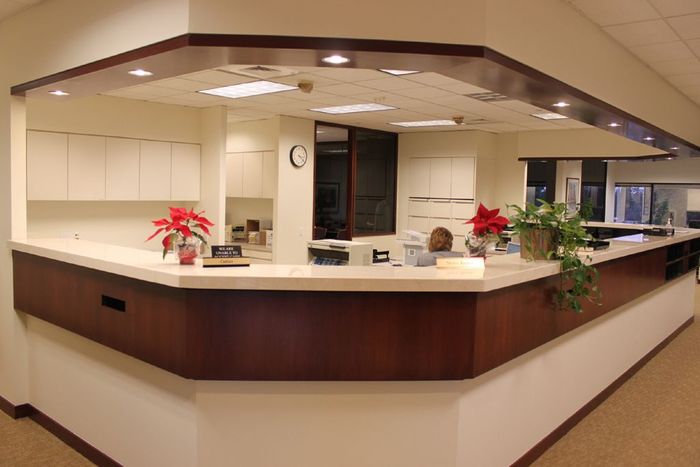 Empty hospital reception desk with beige counters, wood trim, and red poinsettias in a lobby
